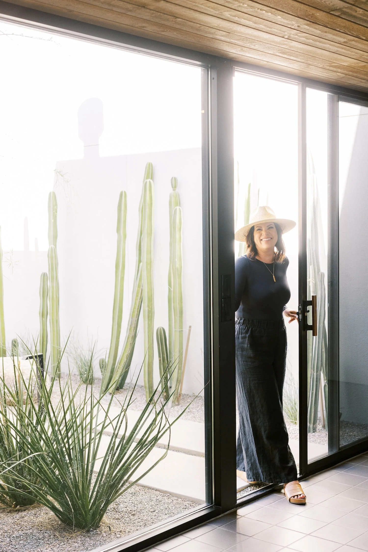 Kathryn stands in a doorway with cacti and plants.