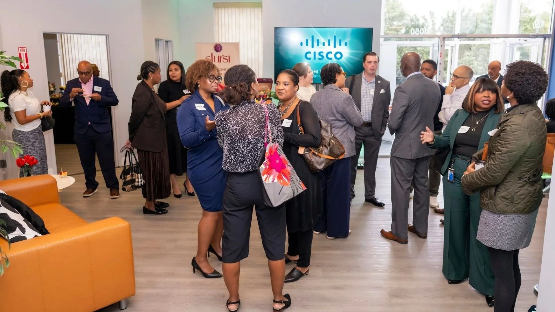 Group of diverse professionals attending a networking event in an office lobby with a Cisco logo on a screen in the background.