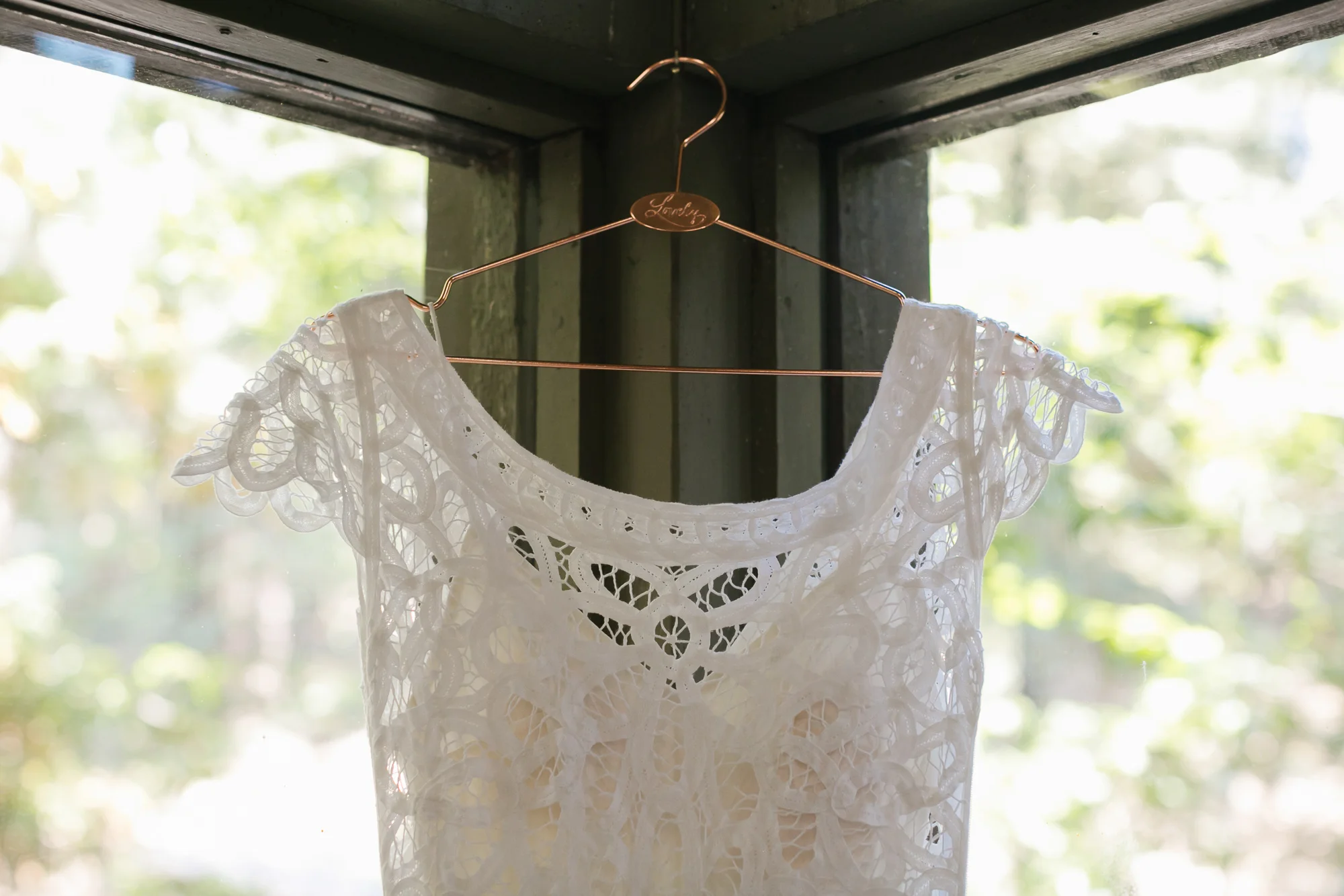Lace wedding dress on copper hanger in front of windows