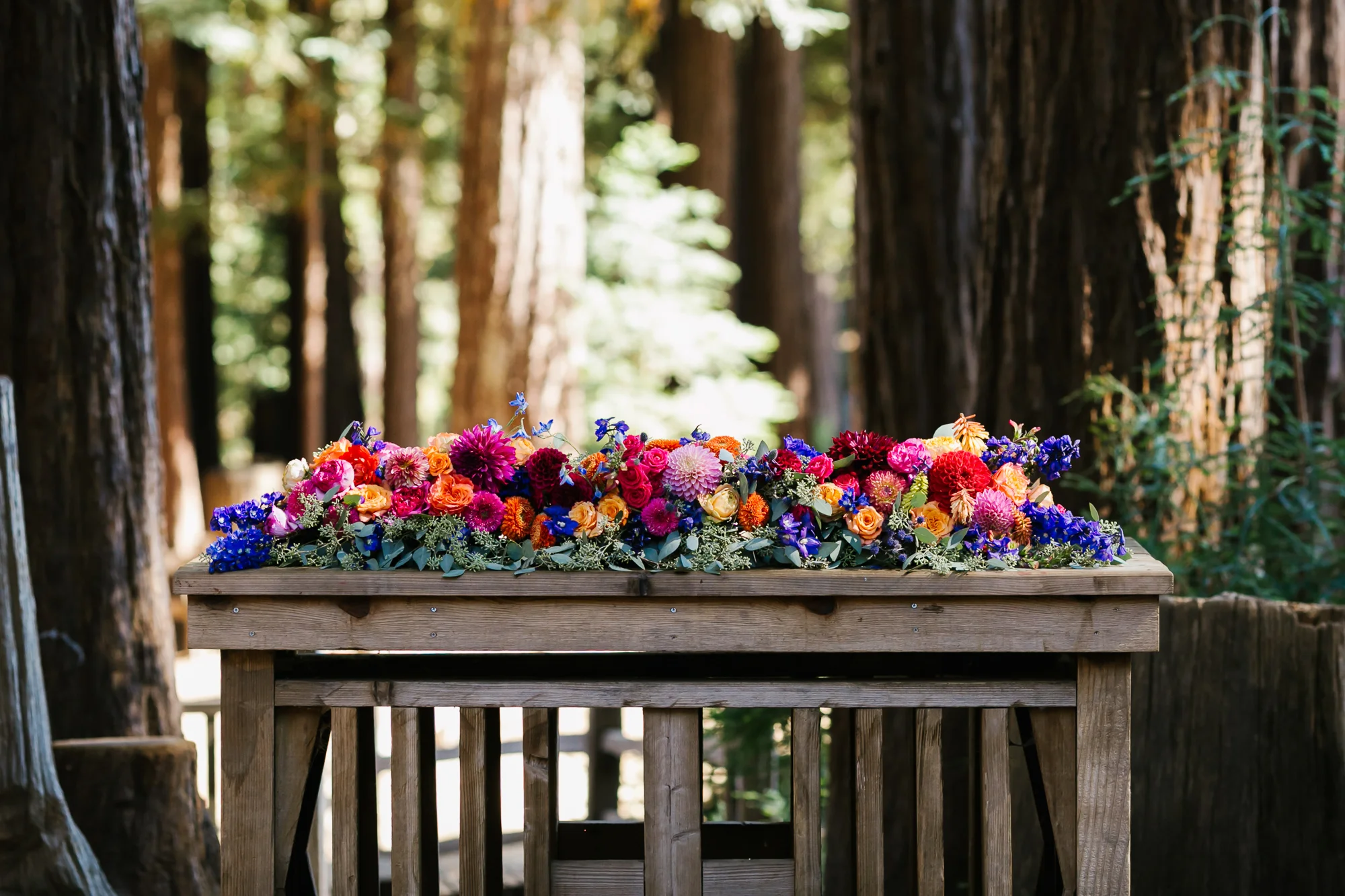Outdoor ceremony altar covered in colorful flowers in redwood forest