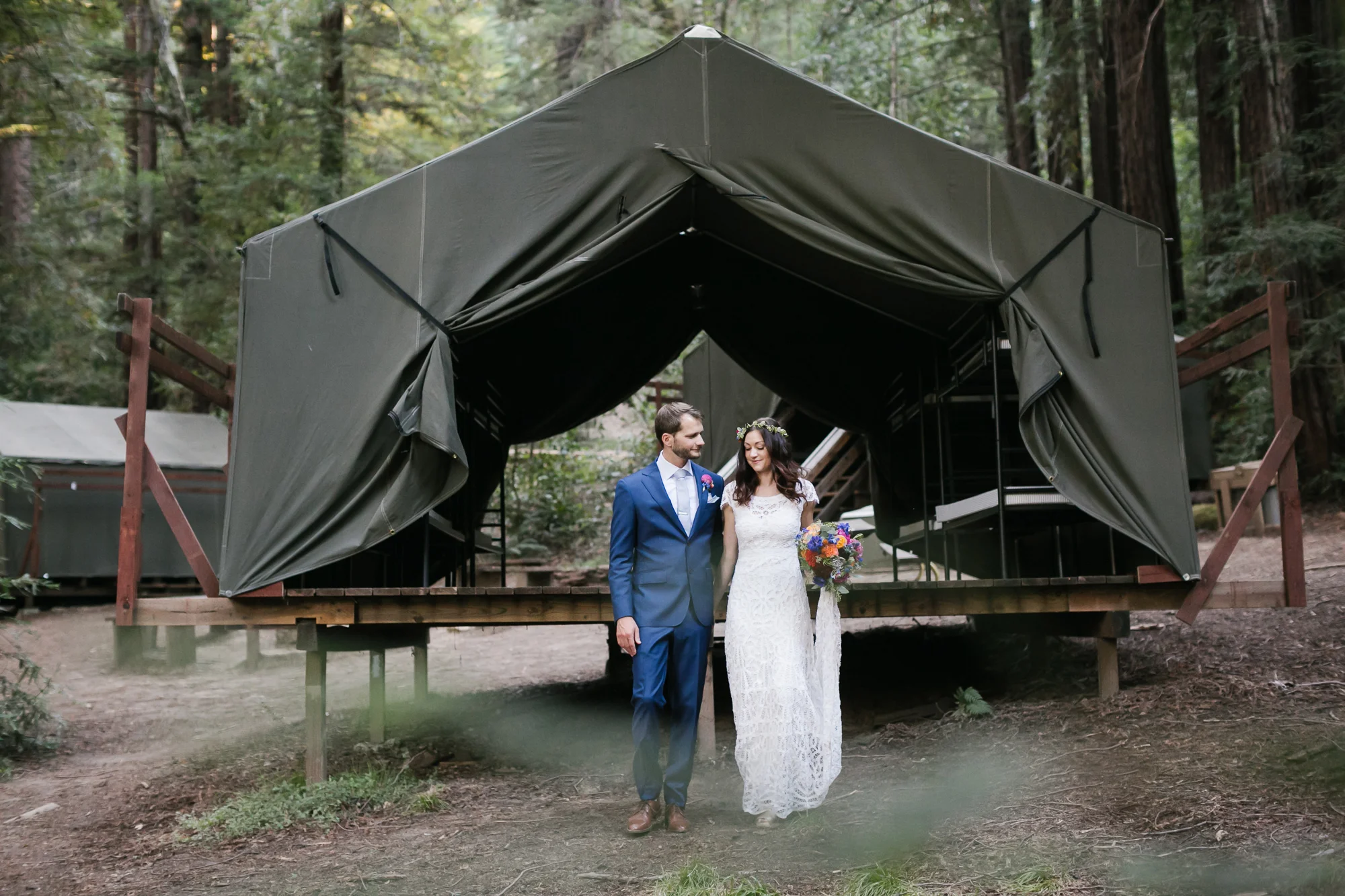 Bright wedding couple stand in front of green canvas tent cabin