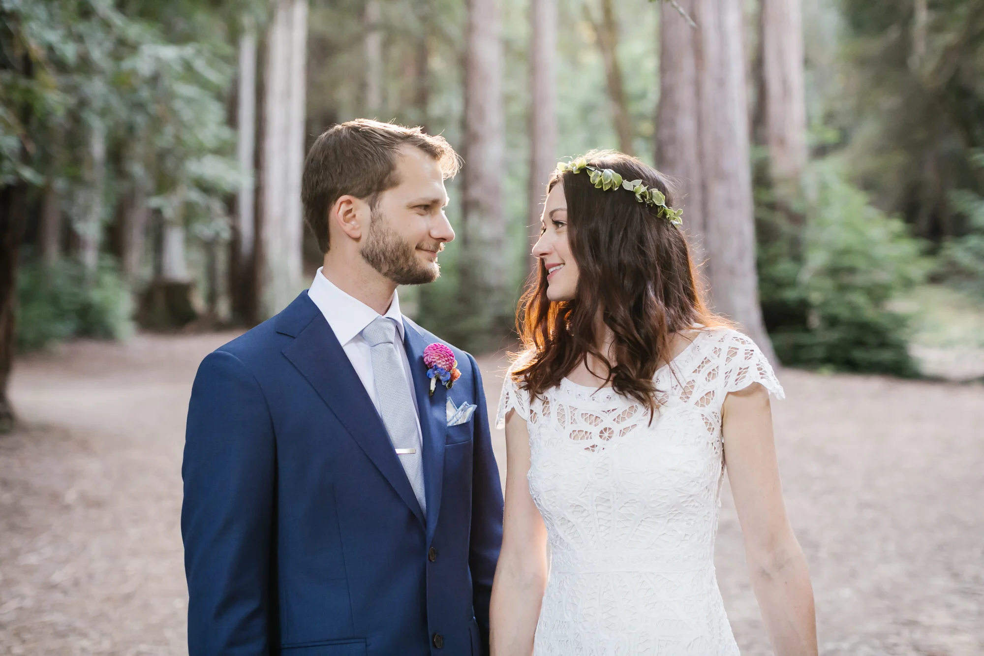 Wedding couple share a look with the sun streaming through the trees