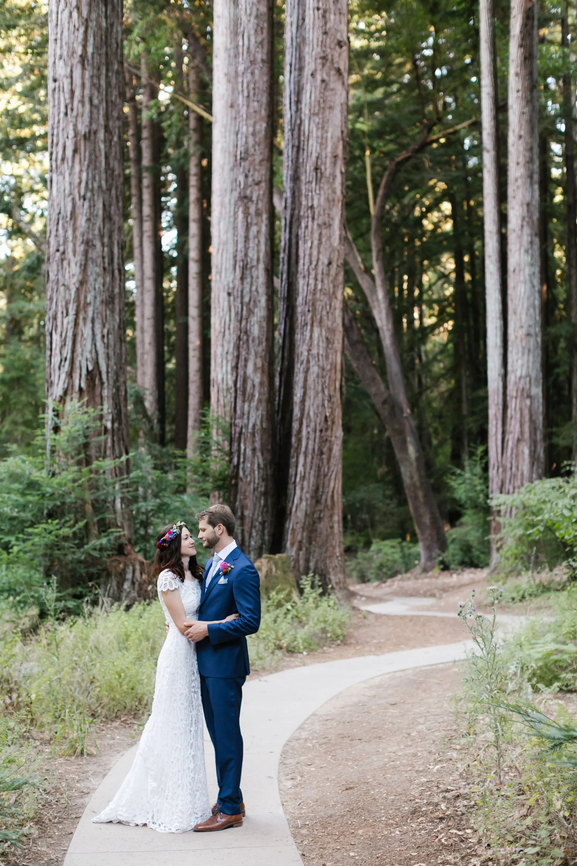 Wedding couple hold each other on winding path through the trees