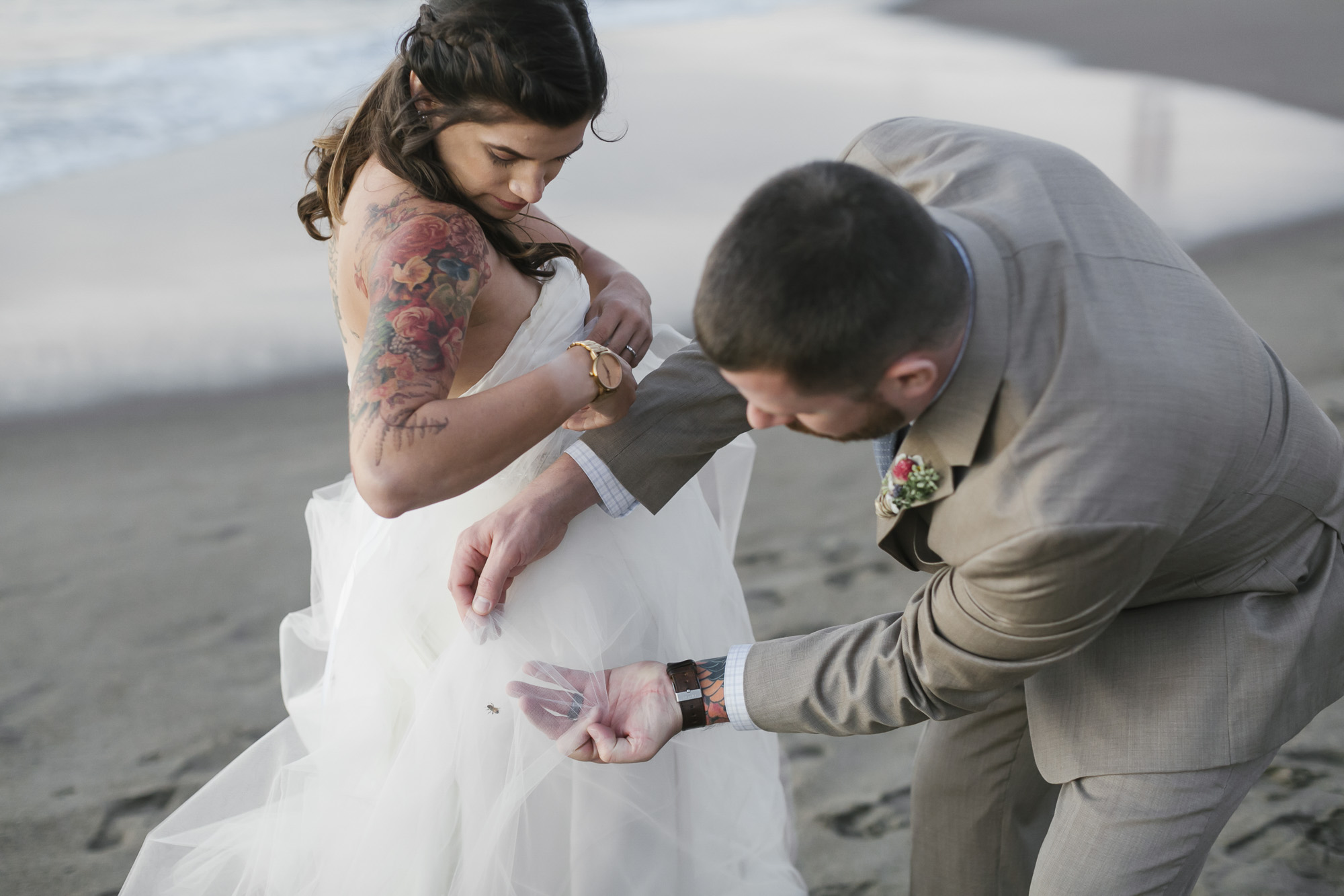Groom helps his bride get a bee out of her dress at Baker Beach