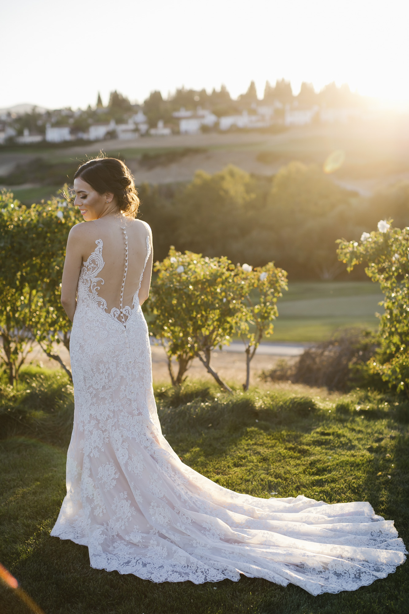 A bride shows off the back of her wedding dress in a garden at sunset