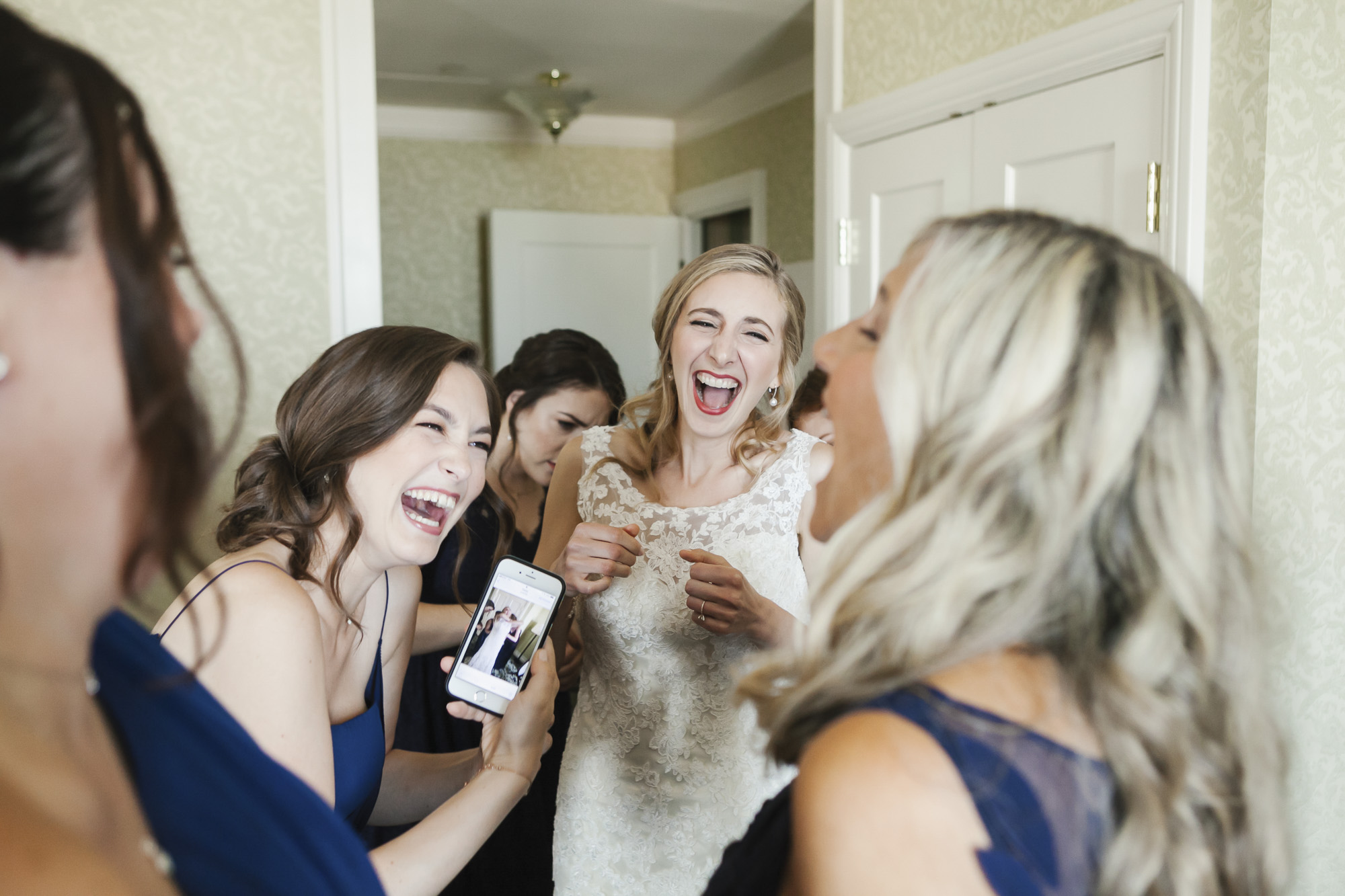 Bride laughs after seeing photo on bridesmaid's phone
