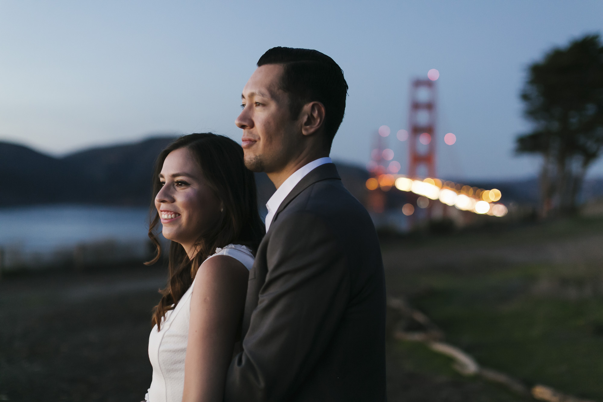 Engaged couple look out at the sunset with the Golden Gate bridge behind them