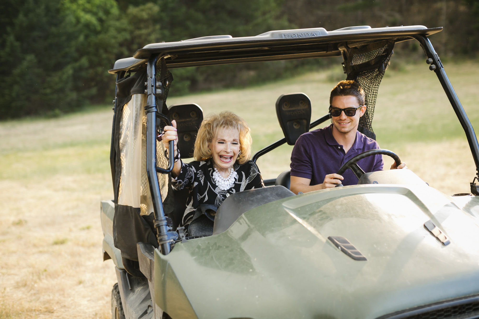 Grandmother laughs while riding shotgun in an ATV with her grandson driving