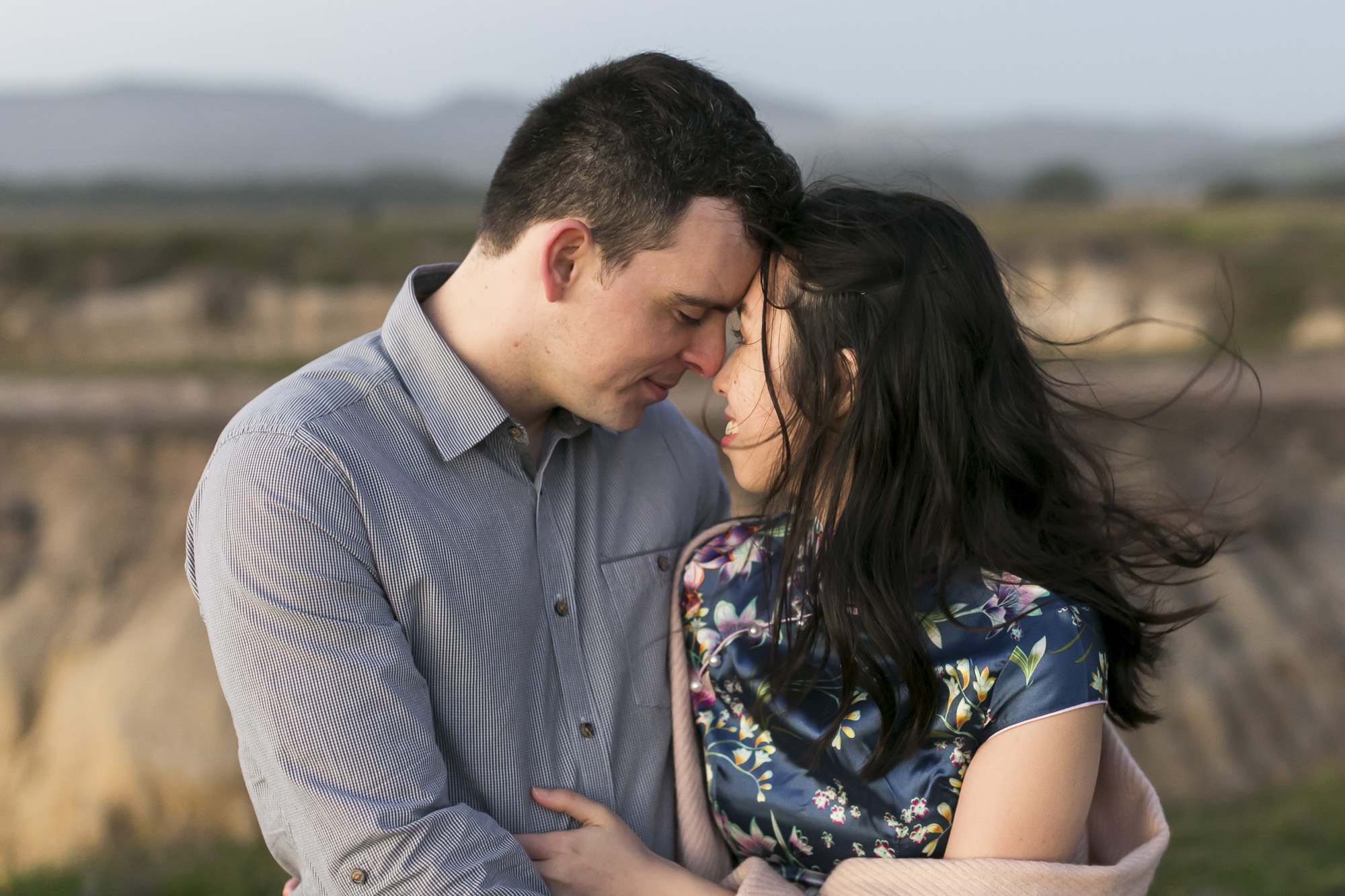 Engaged couple keep each other warm during a windy sunset at Half Moon Bay