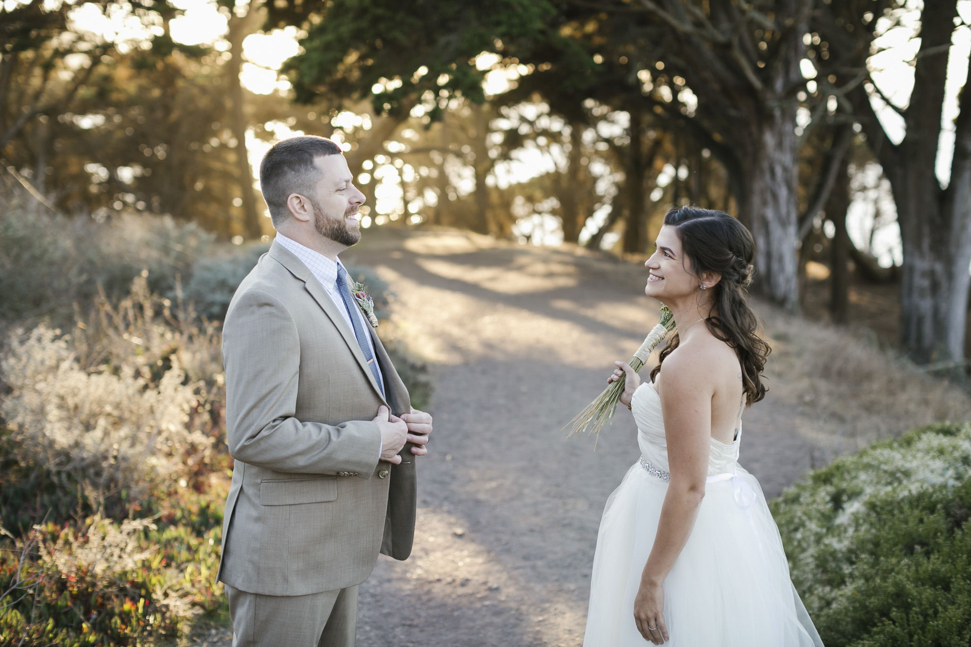 Wedding couple smile at each other as the sun sets behind trees at Baker Beach
