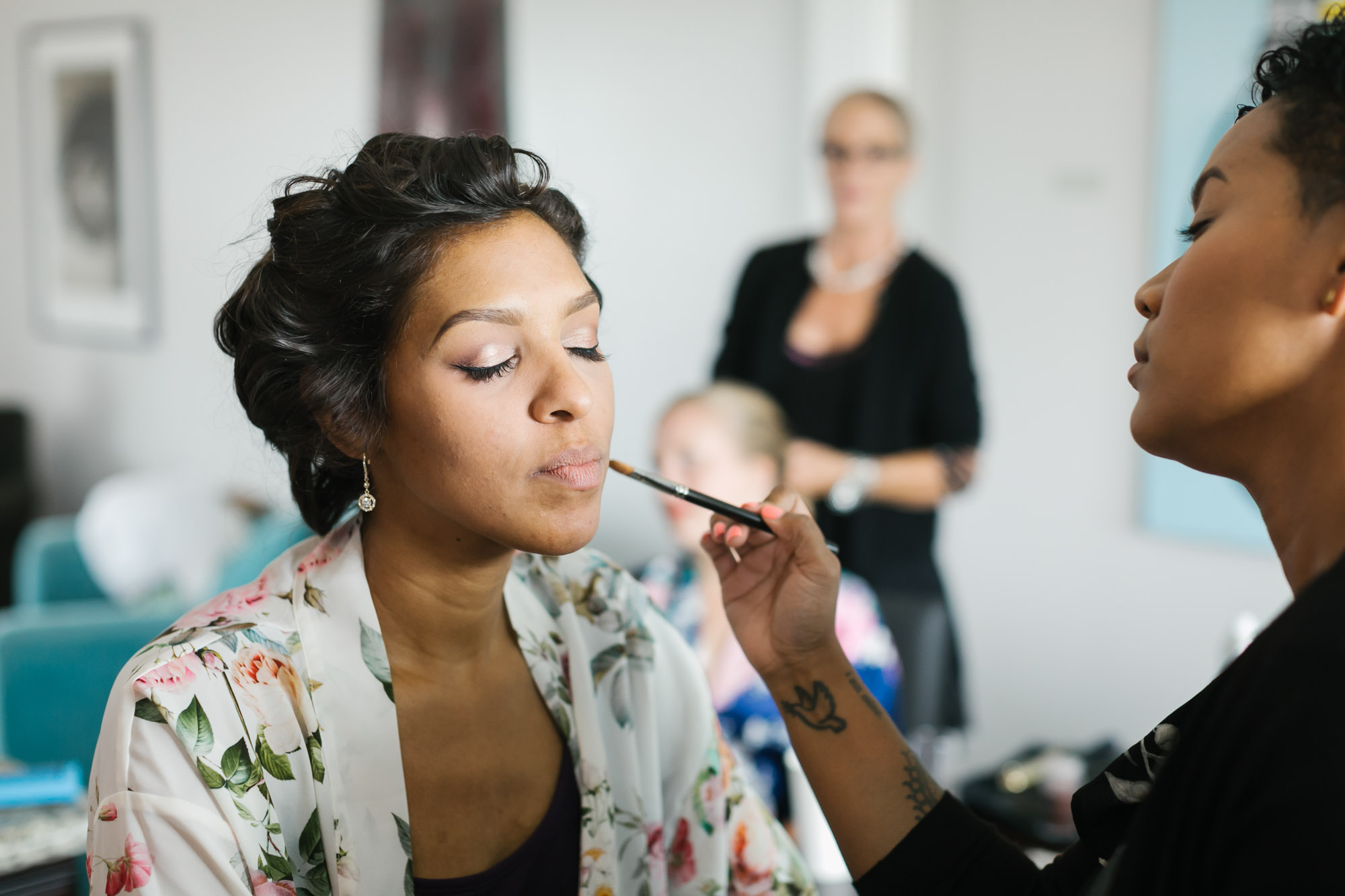 Bride gets her makeup done wearing white floral robe