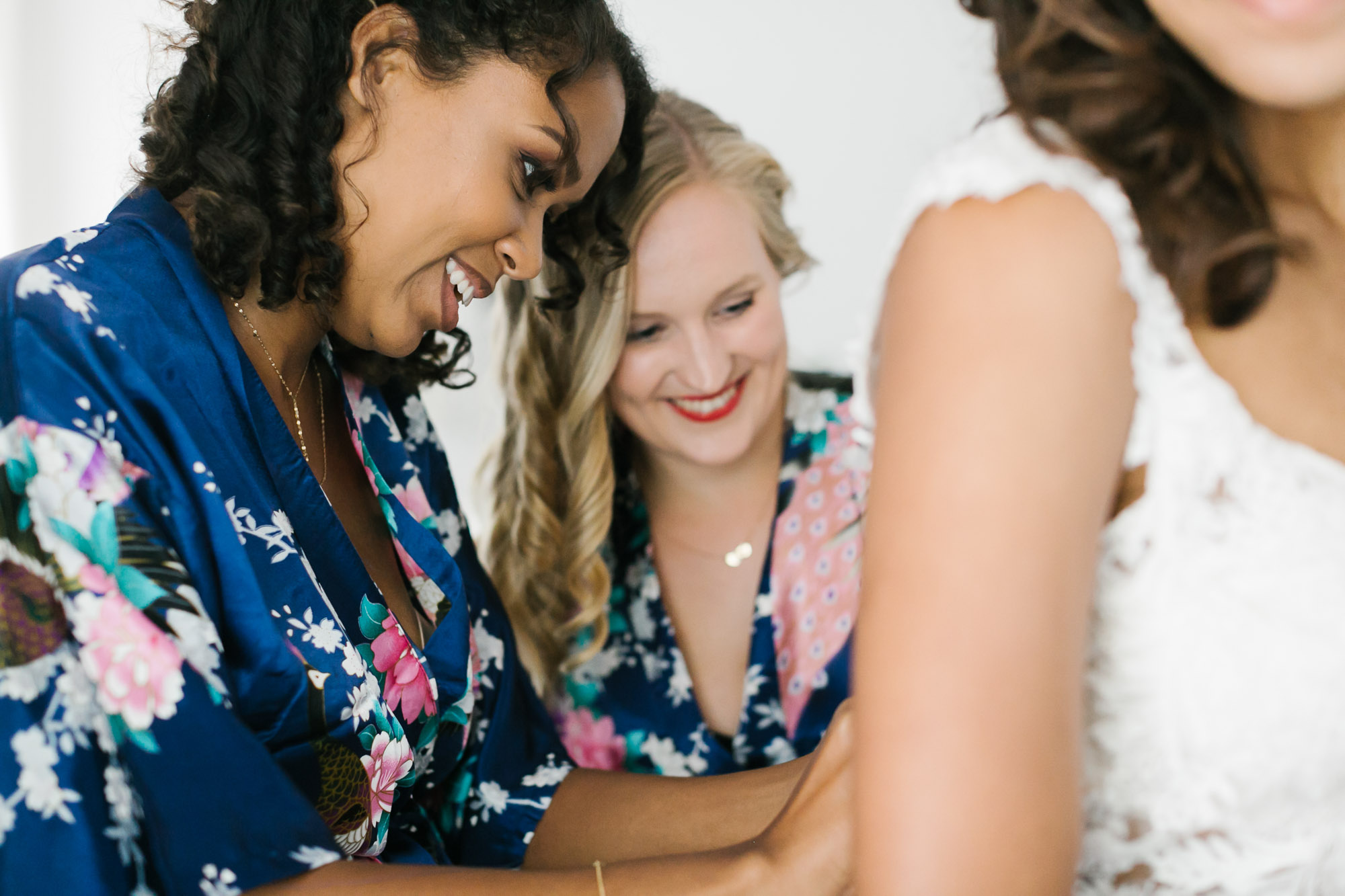 Sisters smile as they help button bride's wedding dress