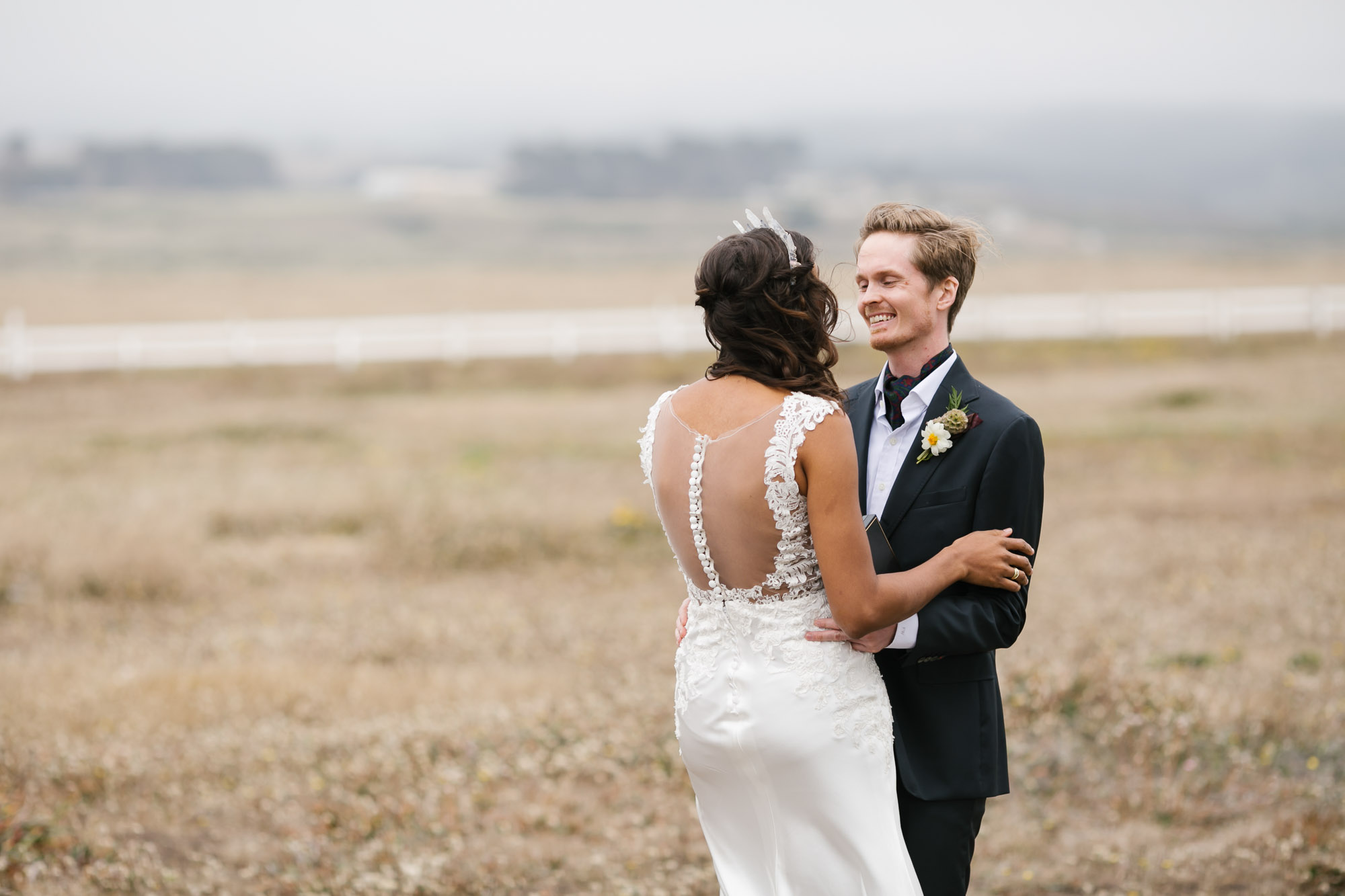 Groom smiles at his bride in a field on the California coast