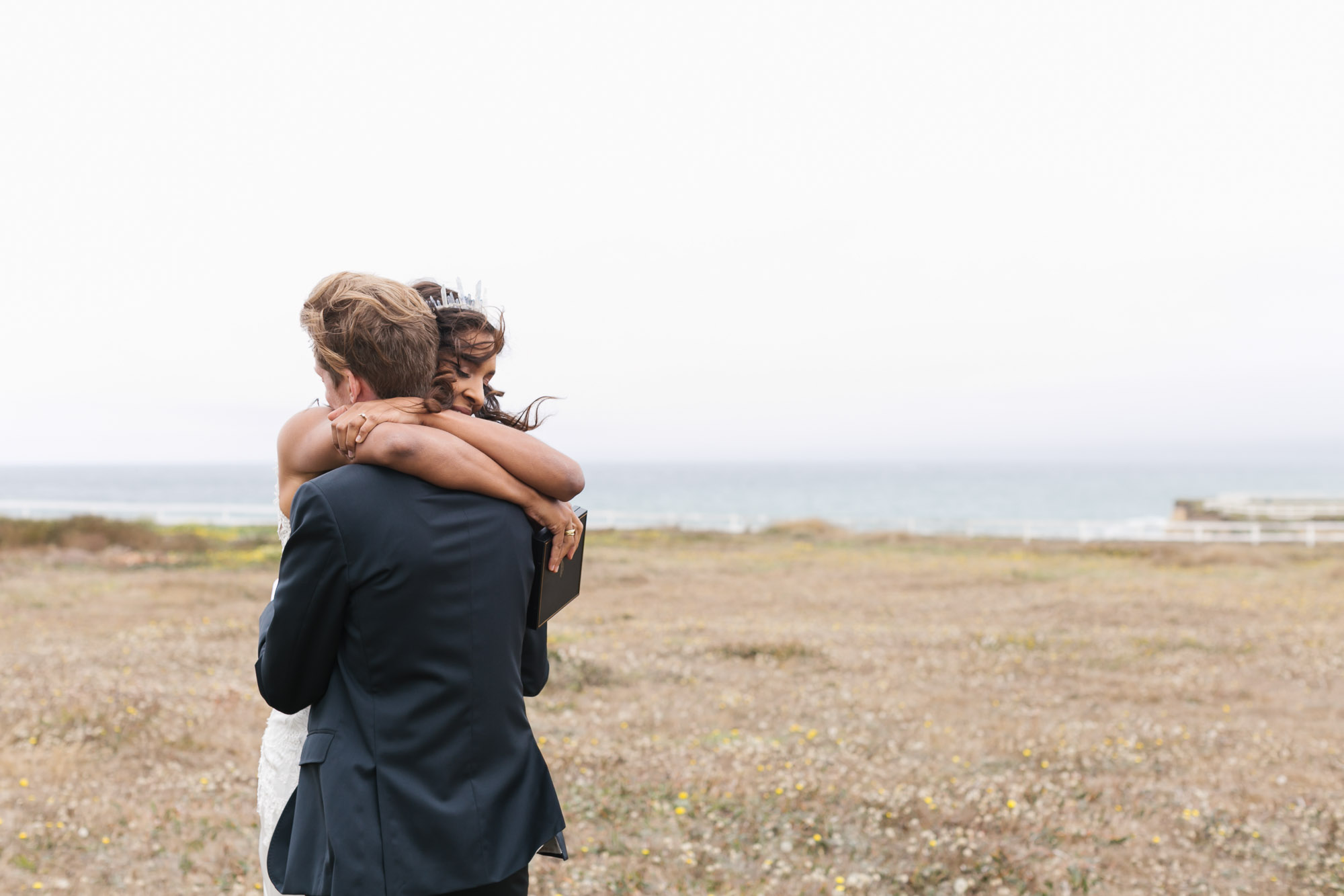Wedding couple hug in meadow along the windy coast of Northern California
