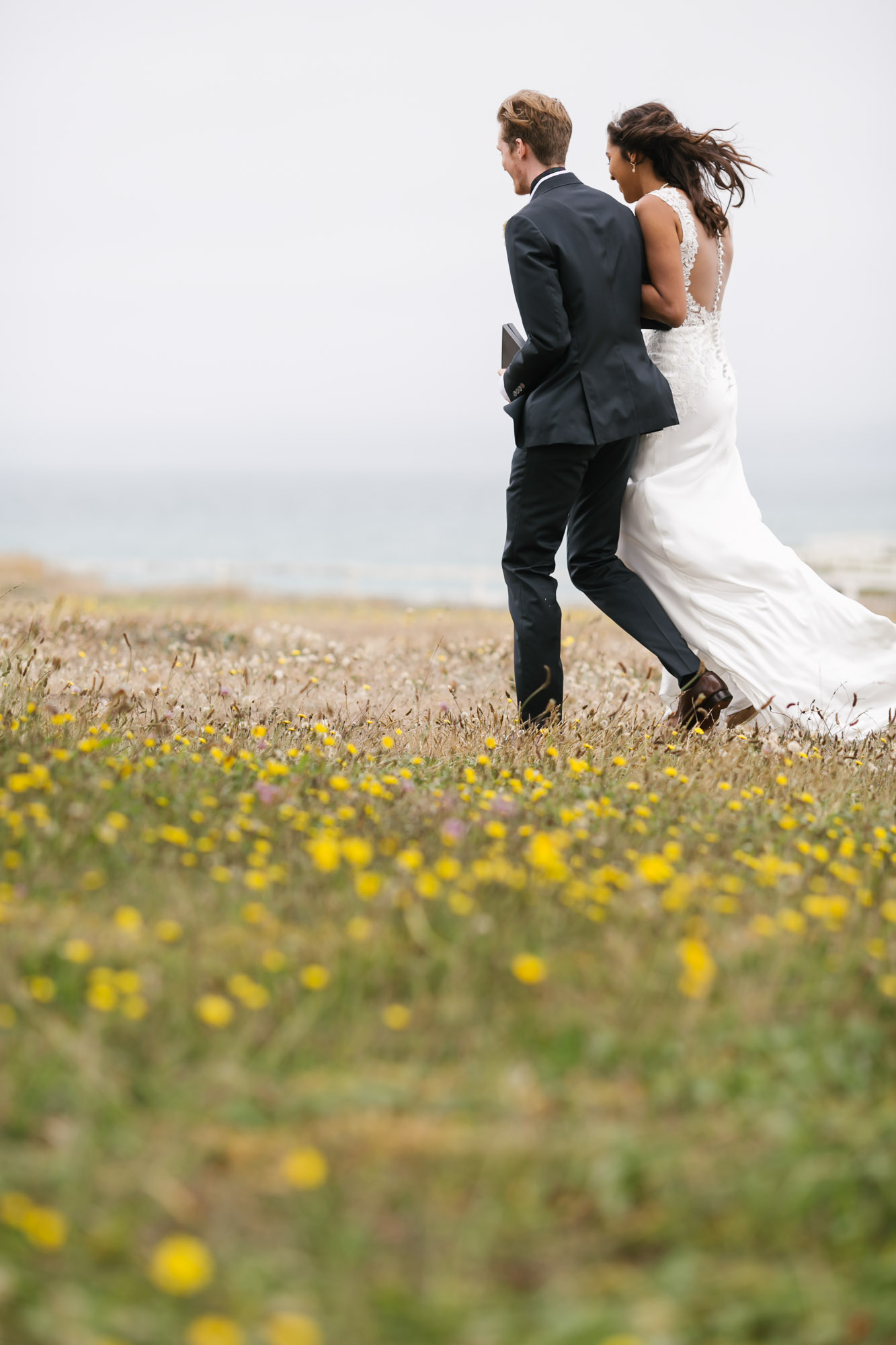 Wedding couple walk away together in field of wildflowers