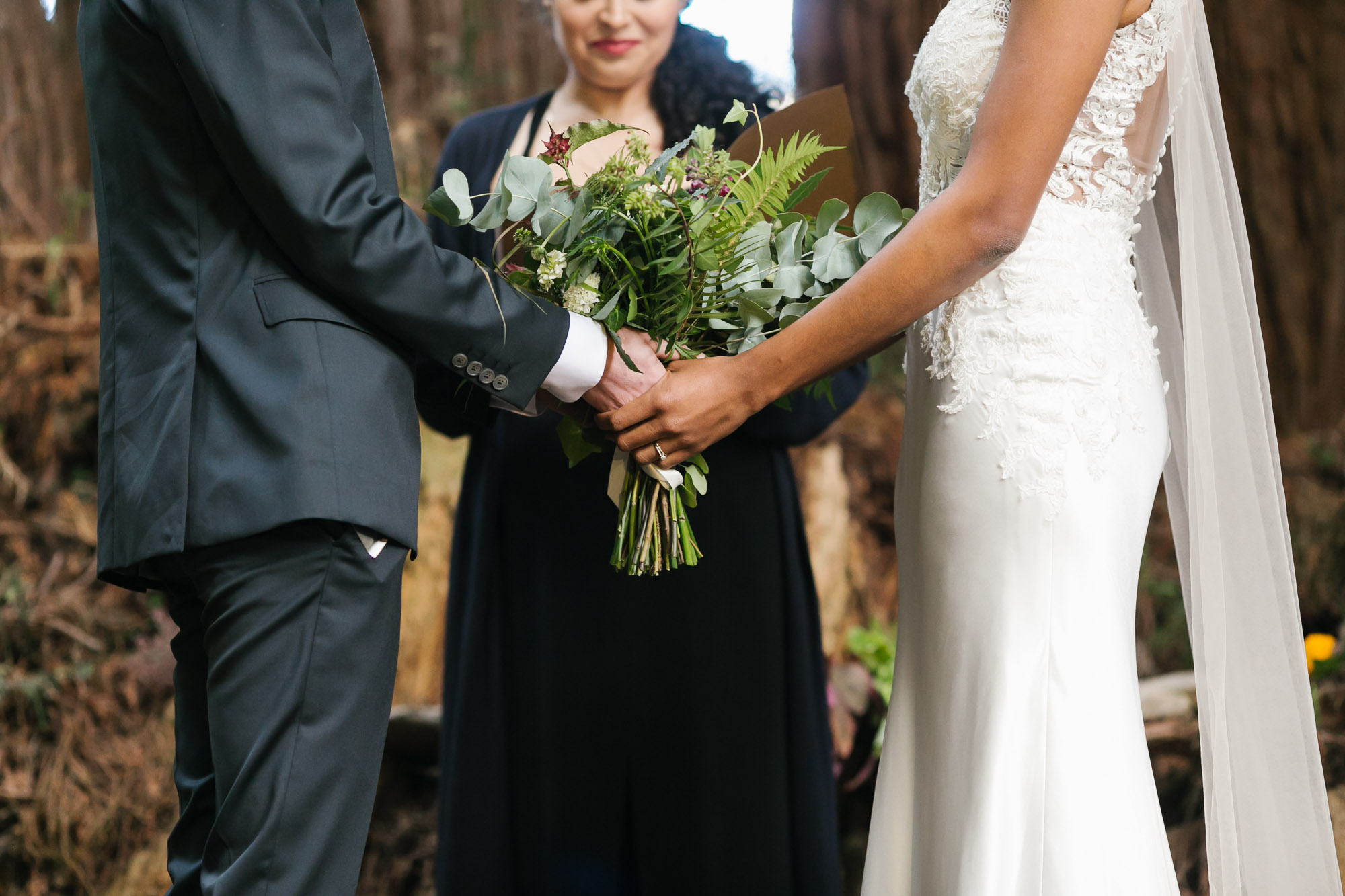 Wedding couple holding bouquet together during ceremony under the trees
