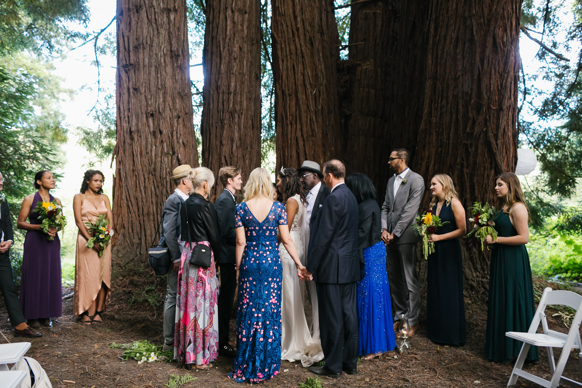 Family surround wedding couple during ceremony in a redwood grove