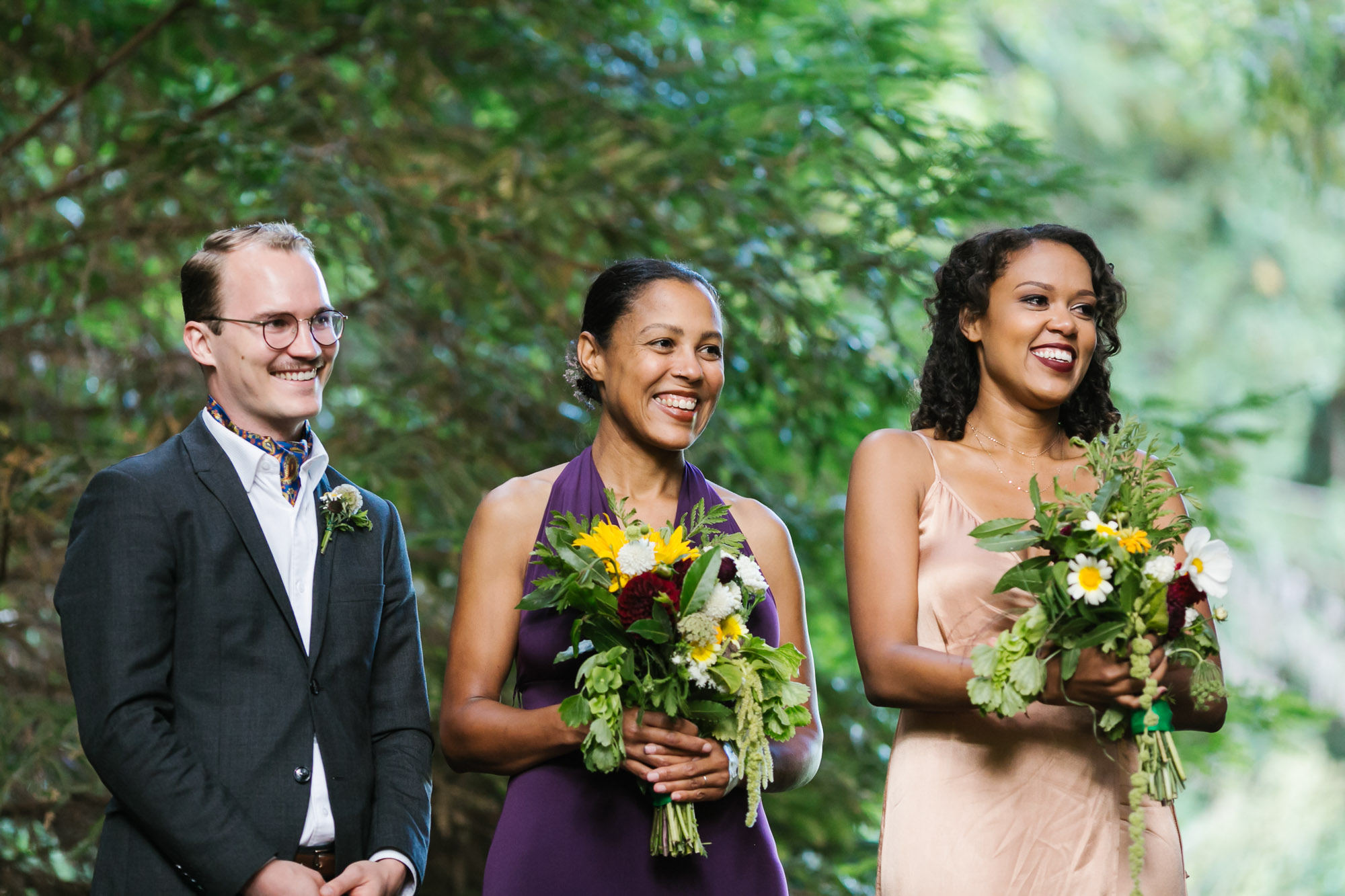 Bridesmaids smile during wedding ceremony holding handmade bouquets