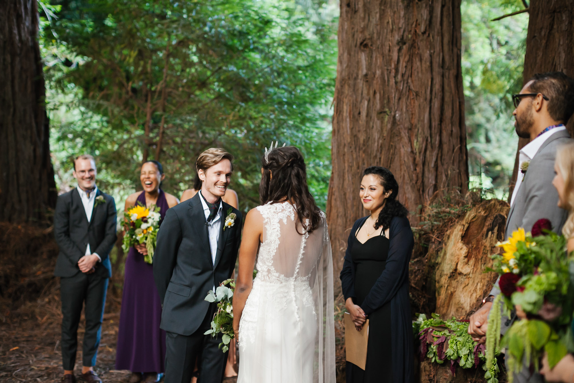 Groom smiles at his bride during ceremony in redwood grove