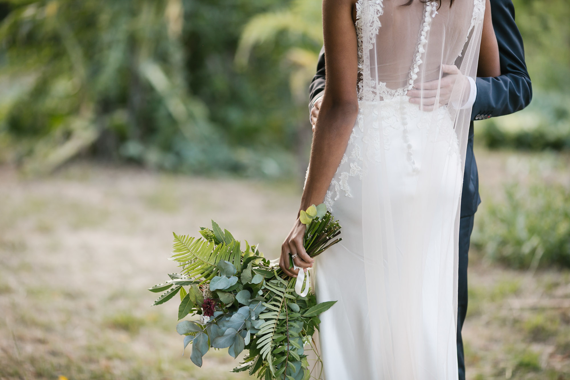 Back of bride's dress showing her veil cape and bouquet