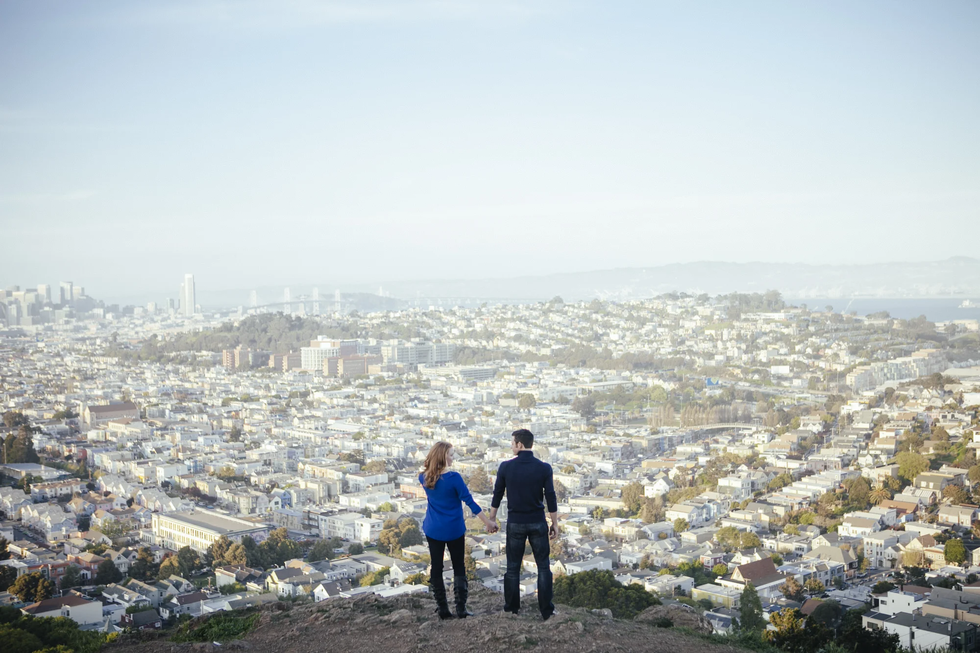 Couple stand in front of the view of San Francisco atop Bernal Heights Park during their engagement portraits.