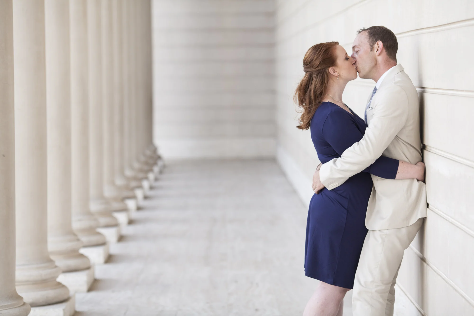 Couple kiss among the columns at the Legion of Honor during their engagement portraits.