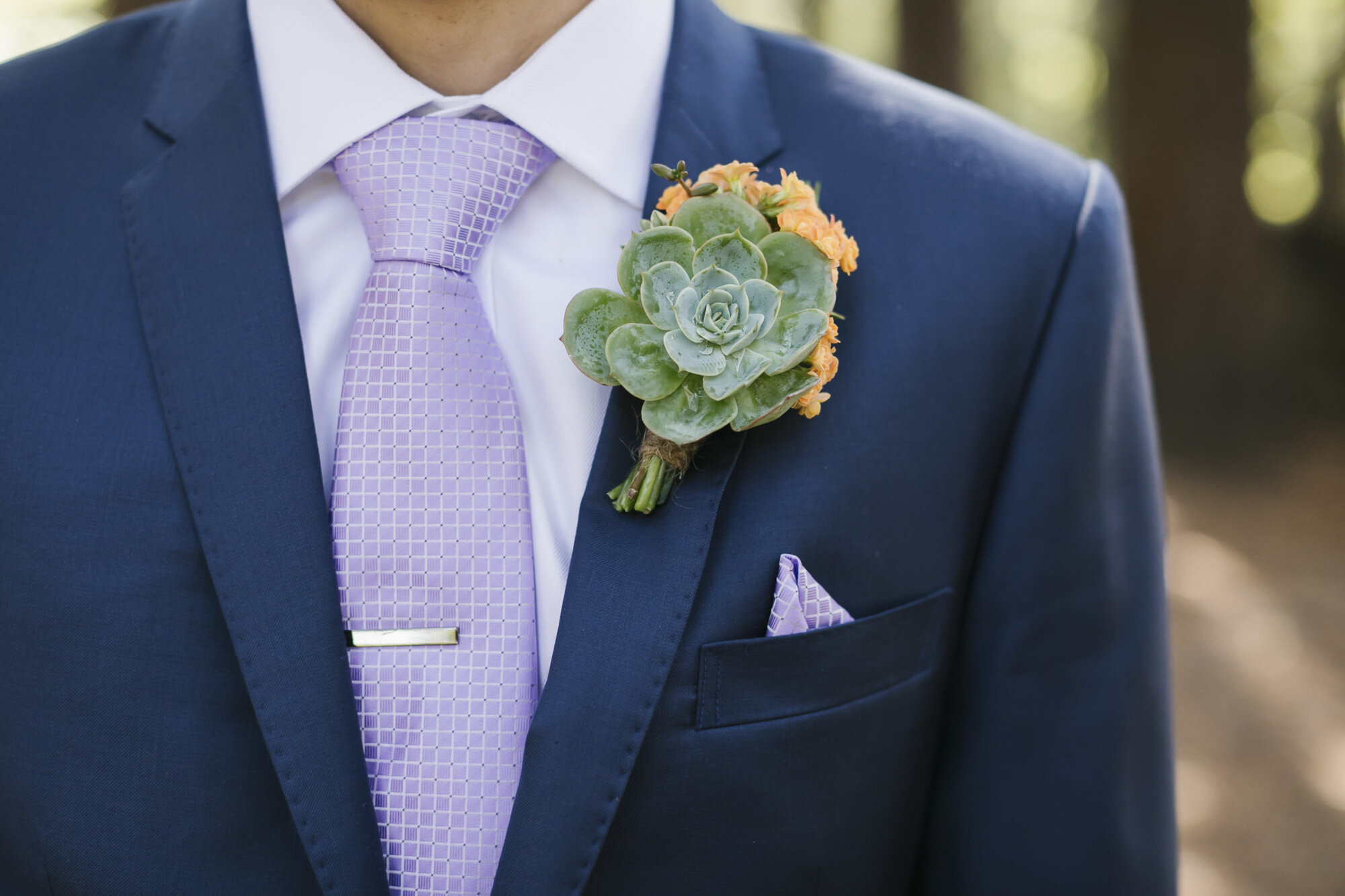 Groom wearing a blue suit with a purple tie and a succulent boutonniere