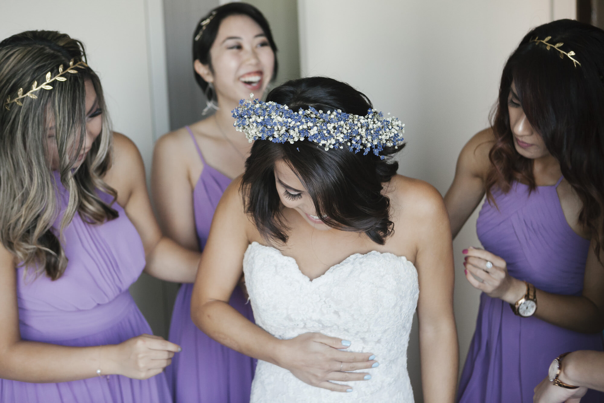 Bridesmaids in purple help bride in flower crown get dressed