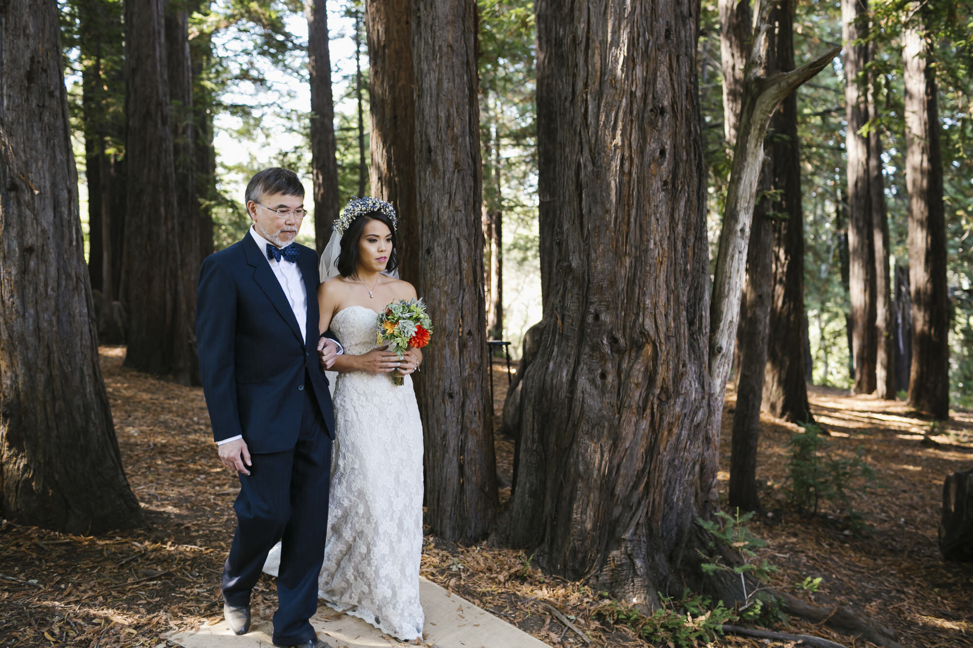 Bride and her dad walk down the aisle in a redwood grove