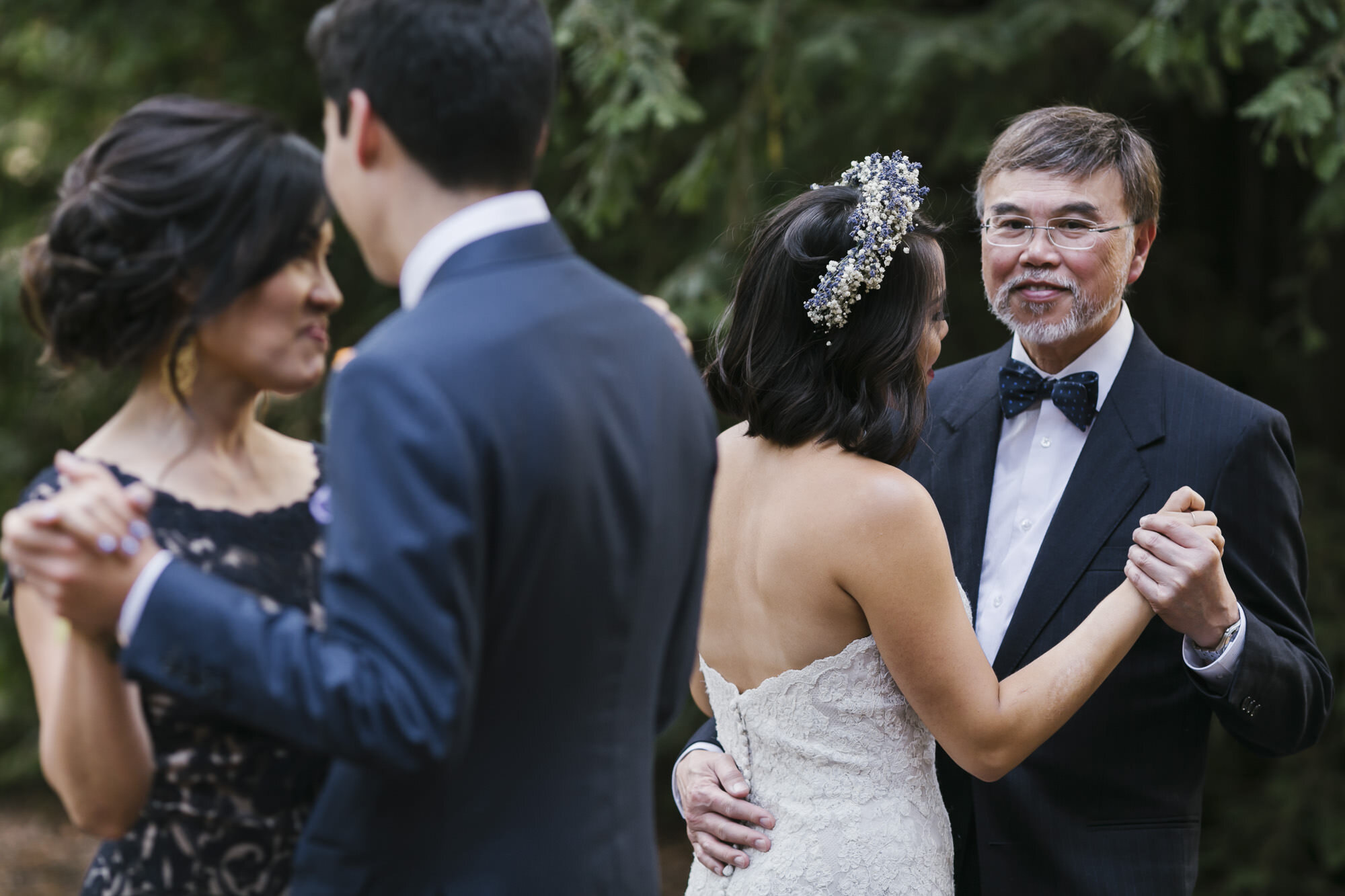 Bride and groom dance with their parents in a redwood grove