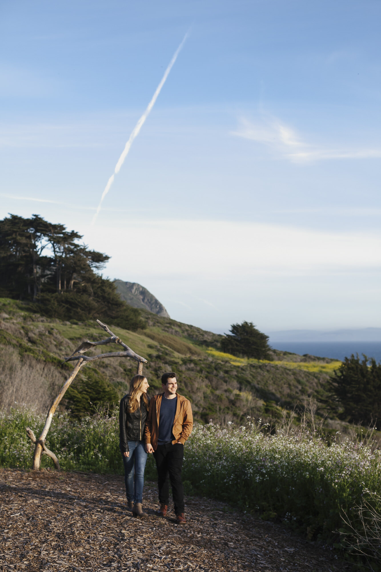Engaged couple stand in front of driftwood arch at Slide Ranch on the coast of California
