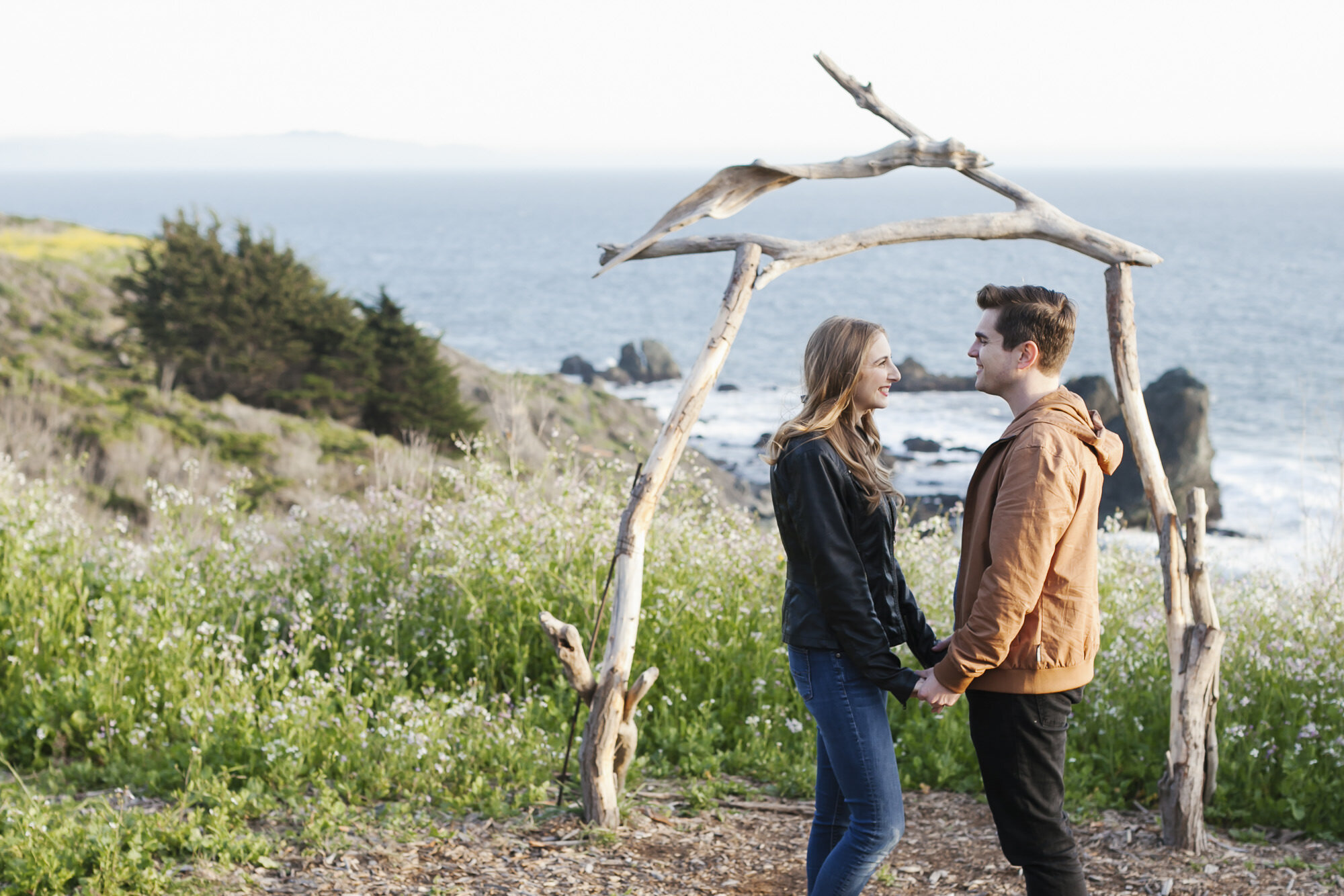 Engaged couple stand in front of driftwood arch at Slide Ranch on the coast of California