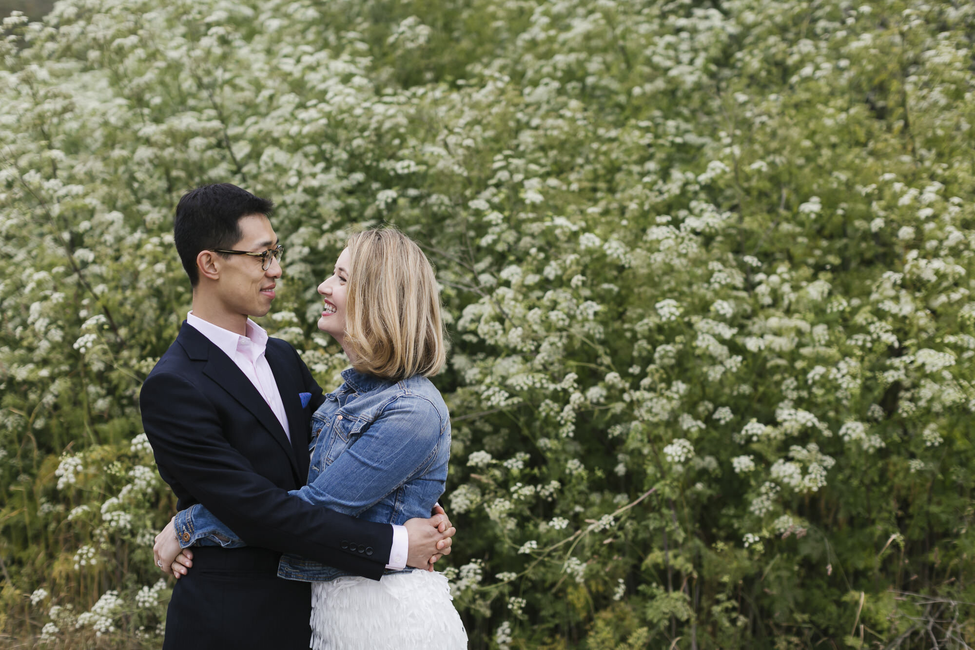 Couple hug in front of wall of white wildflowers