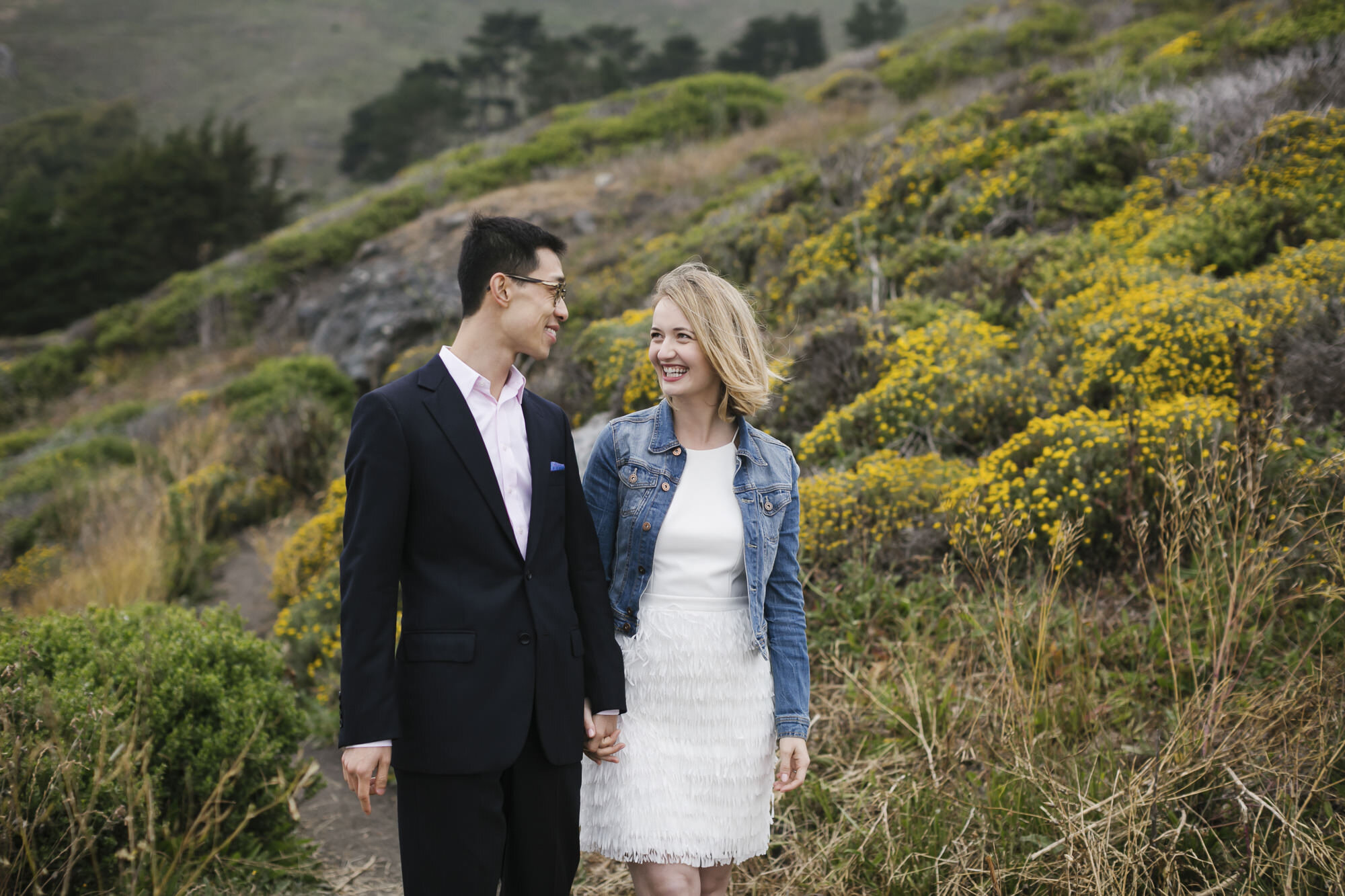 Married couple smile as they walk down a trail on the California coast together