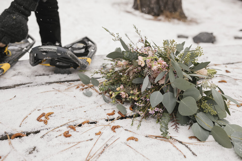 Eucalyptus and pink rose wedding bouquet lays on a snowy picnic table