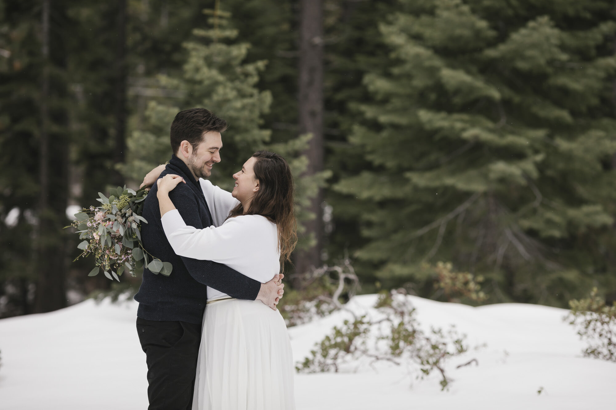 Wedding couple hug in a snowy forest on their elopement day in winter in Lake Tahoe