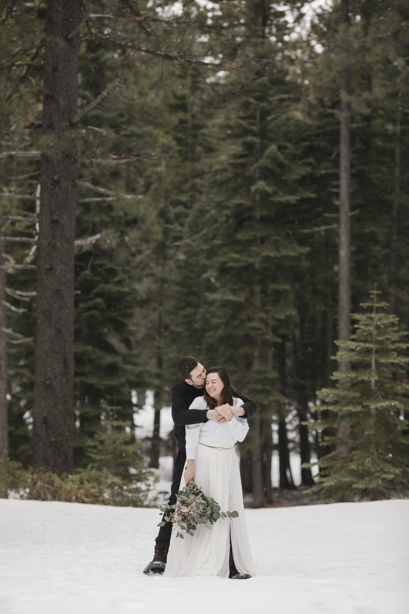 Groom kisses his bride while she laughs during their elopement day in the snow in Lake Tahoe