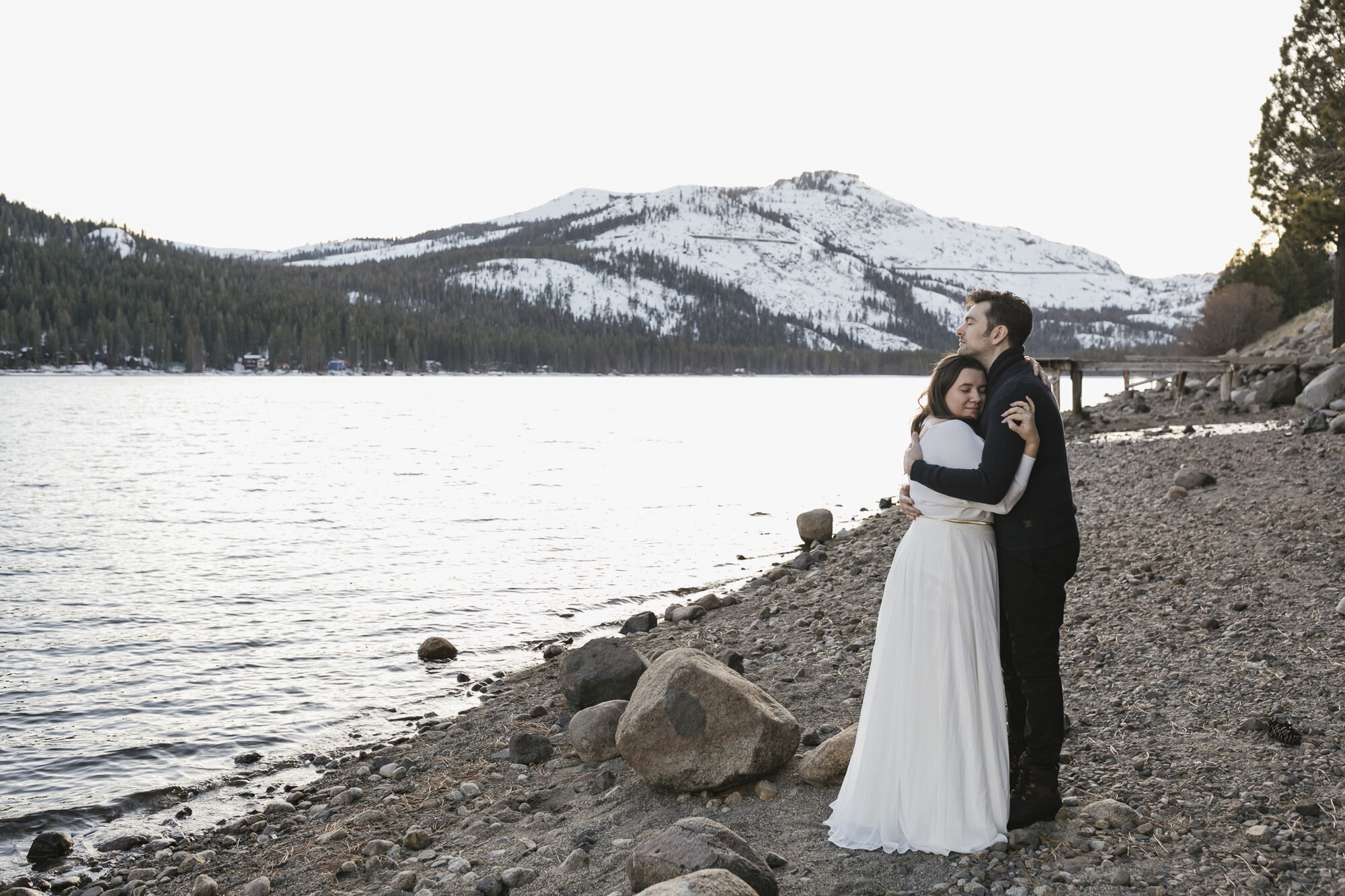 Wedding couple hug each other lakeside at Donner Lake with the snowy summit in the background