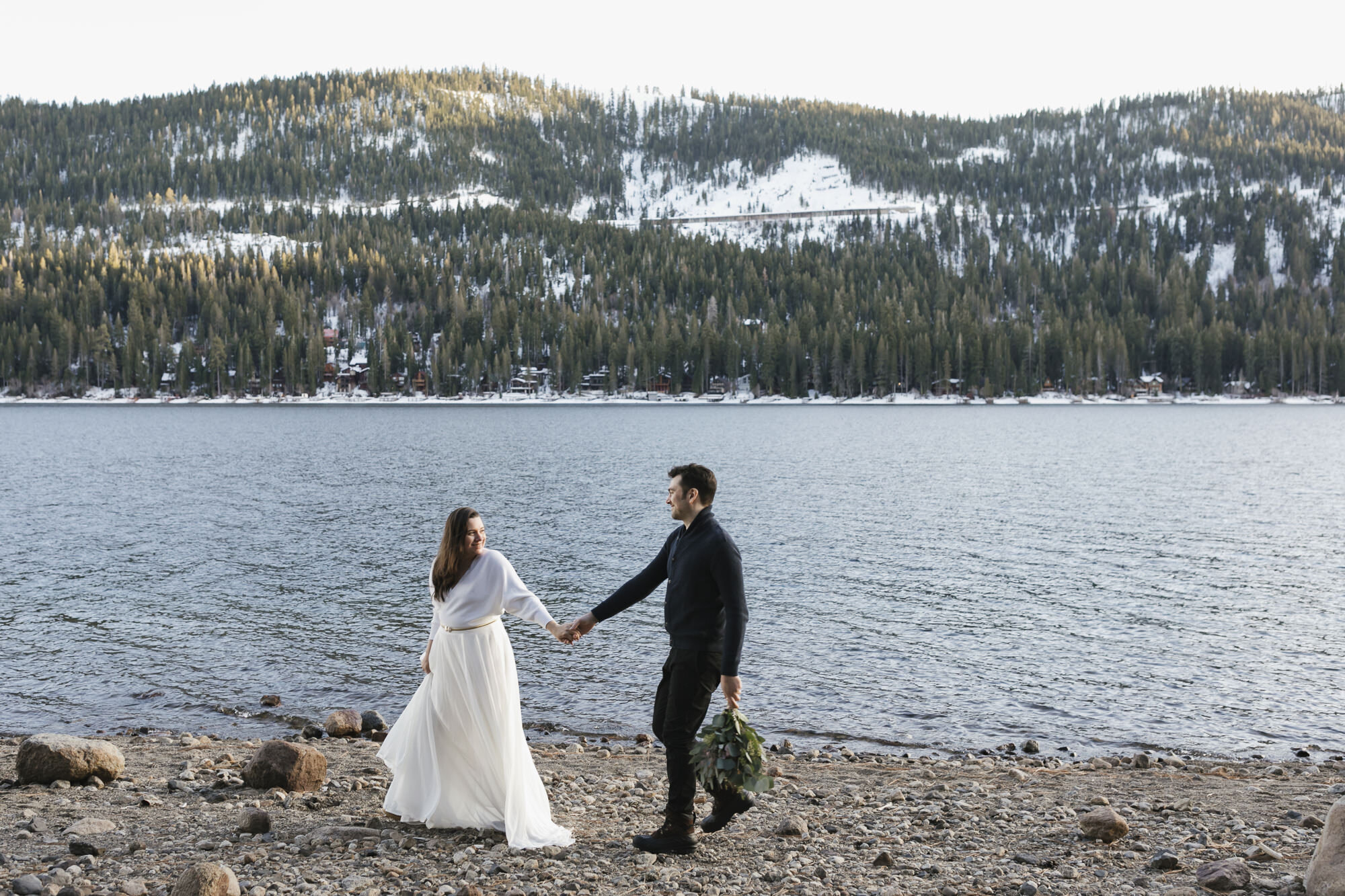 Bride leads groom to walk along Donner Lake during their winter elopement