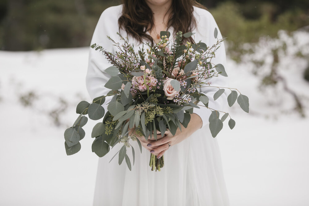 Bride holds her eucalyptus and pink rose wedding bouquet in the snow