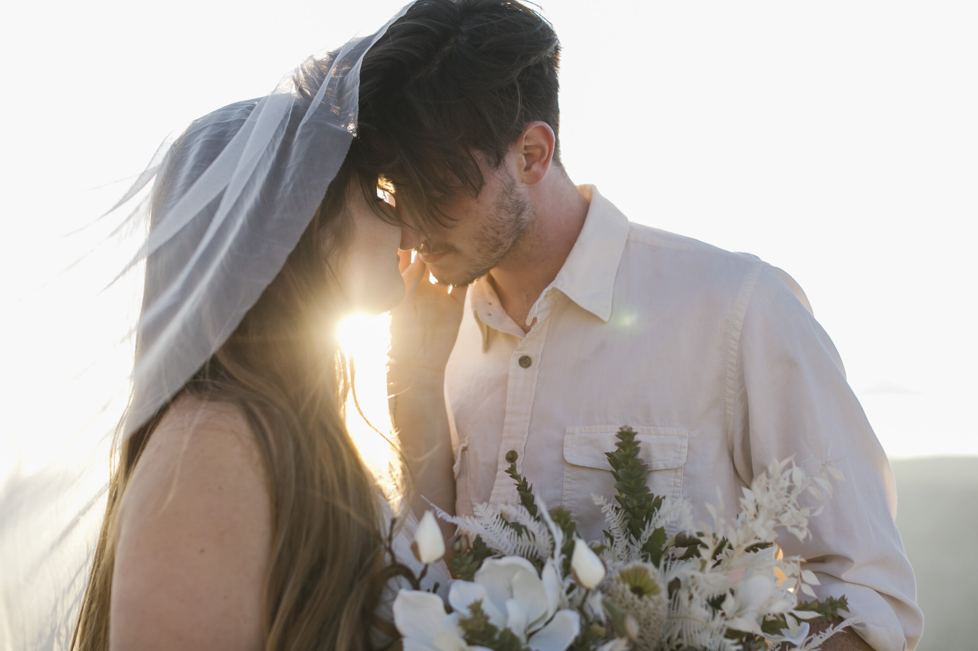 Elopement couple go in for a kiss with the sun setting in between them