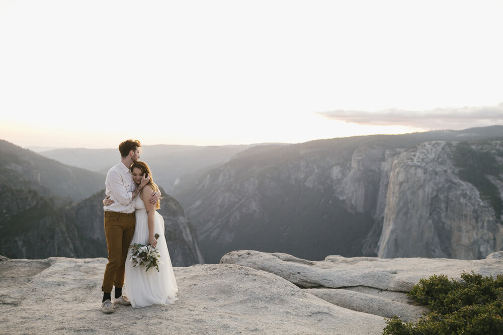 Bride and groom hug at Taft Point with the sun setting behind them in Yosemite