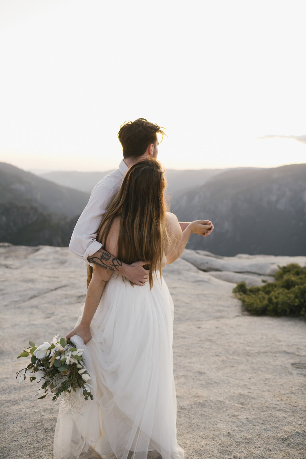 Groom holds his bride as they enjoy the sunset over Taft Point in Yosemite