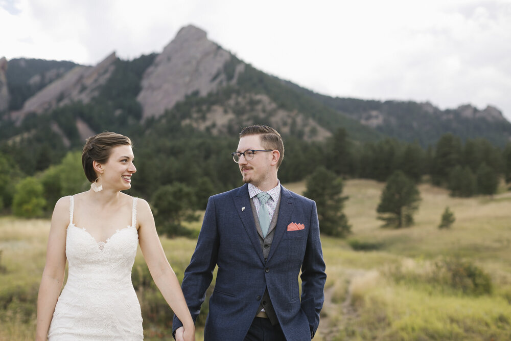 Elopement wedding couple walk holding hands with the Flatirons behind them