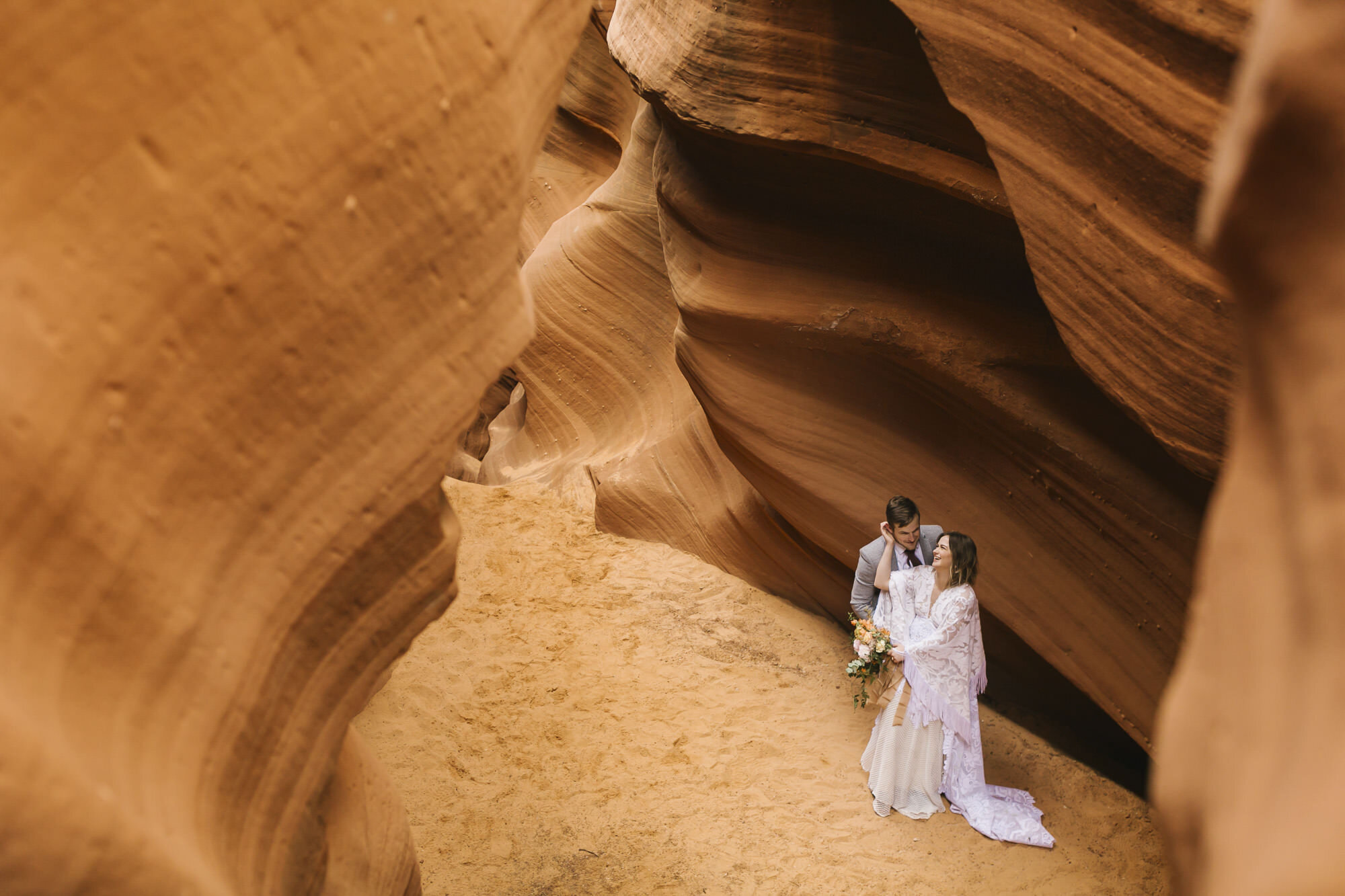 Looking down on a snuggly wedding couple in a slot canyon in the desert in Arizona
