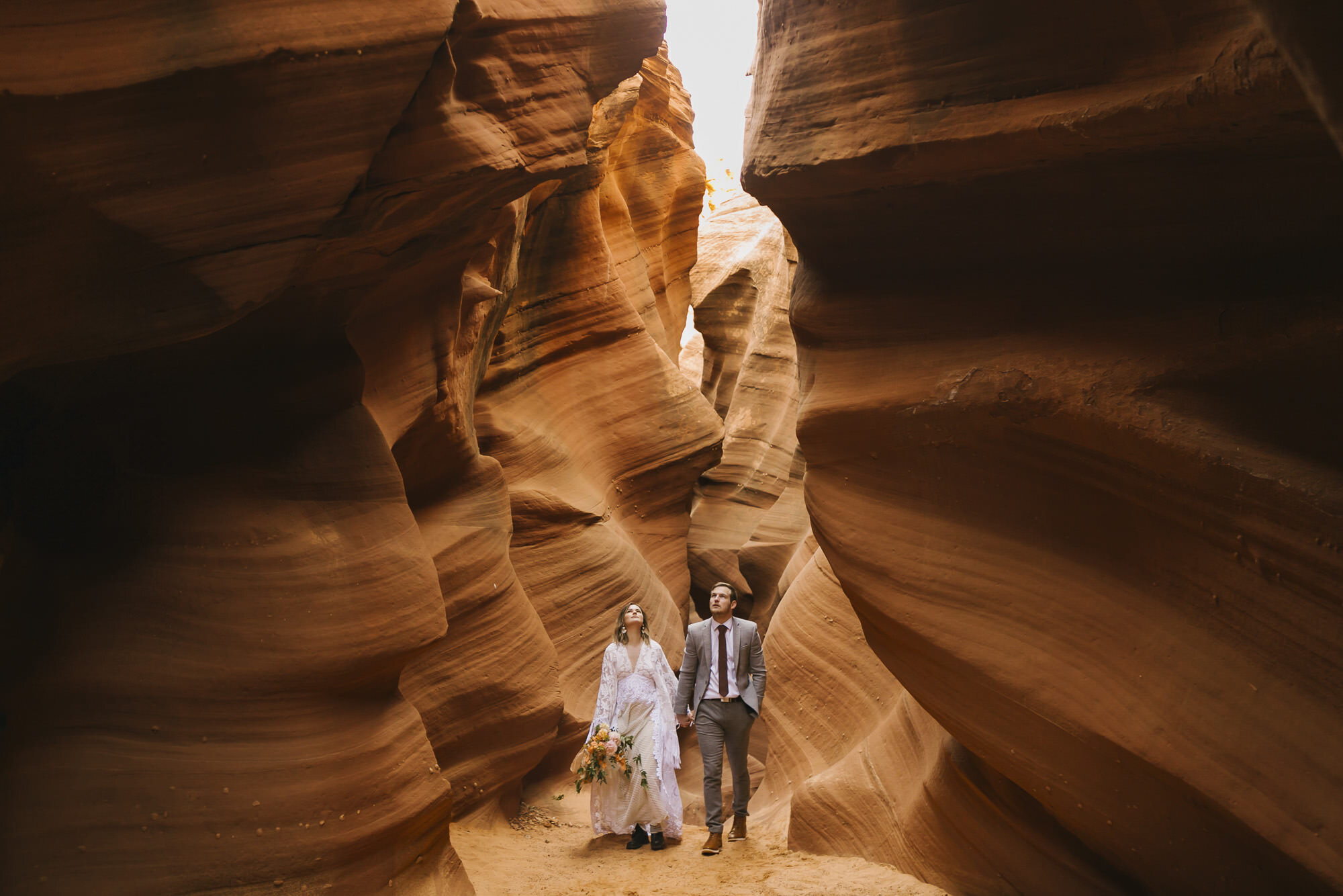 Wedding couple look up as they walk through an Arizona slot canyon