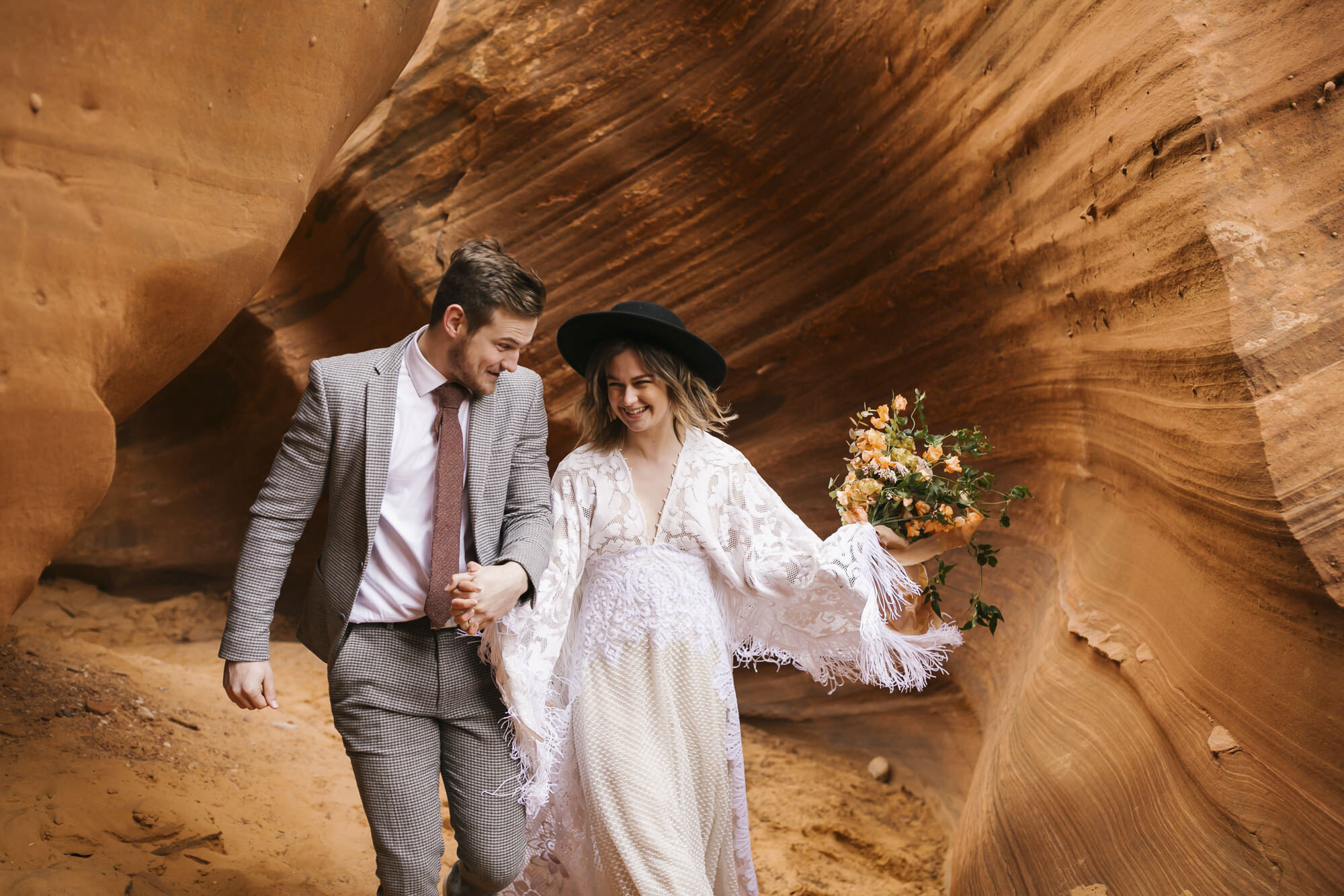 Wedding couple run through the end of a slot canyon in the Arizona desert