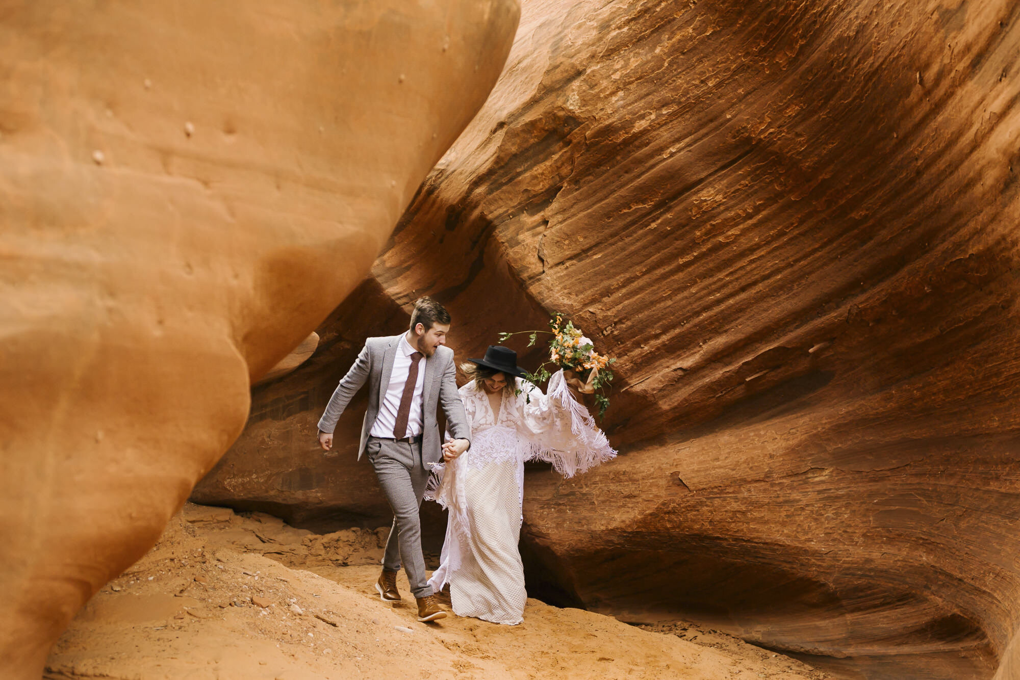 Wedding couple joyfully run through the end of an Arizona slot canyon