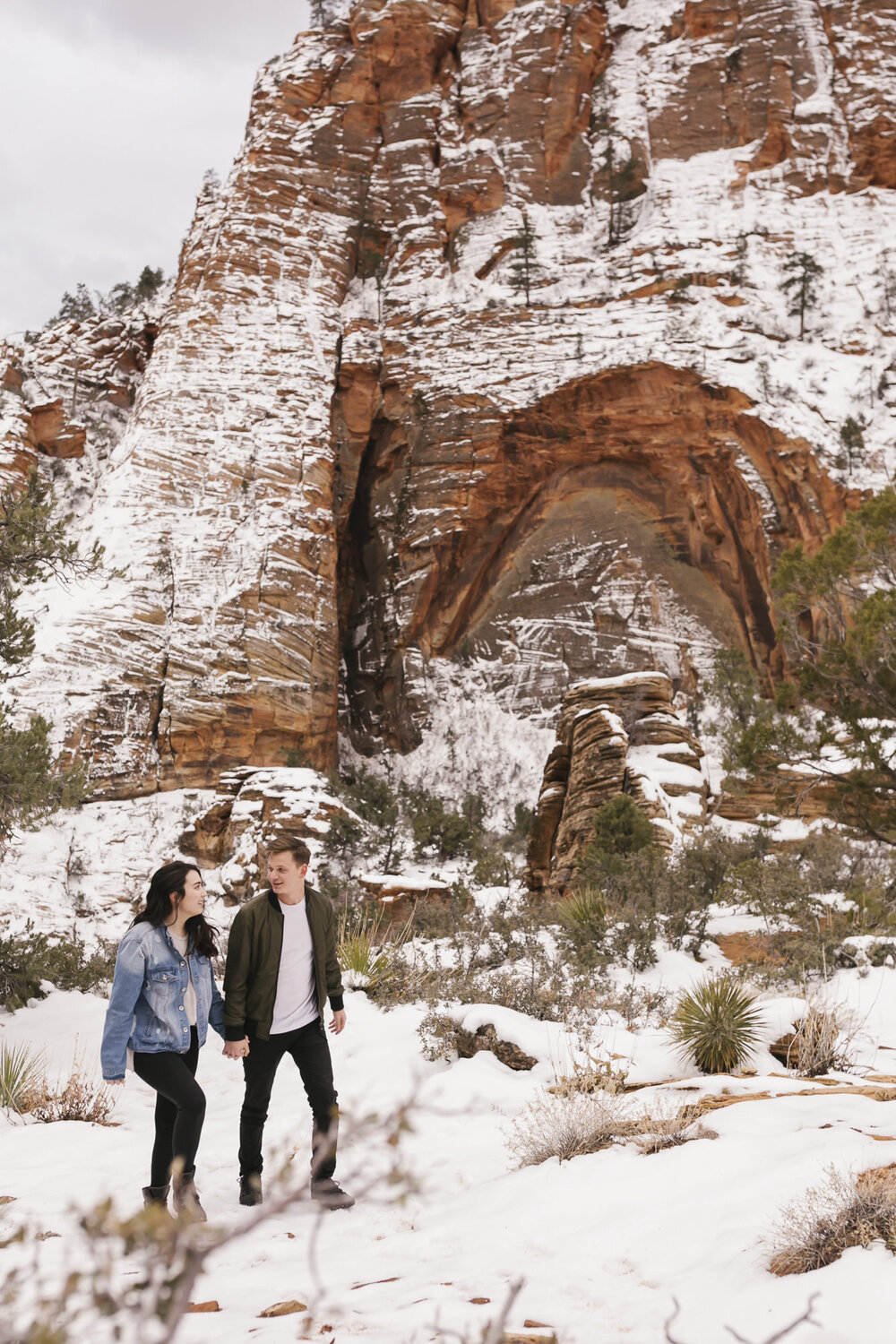 Adventurous couple hike holding hands through the snow together in Zion