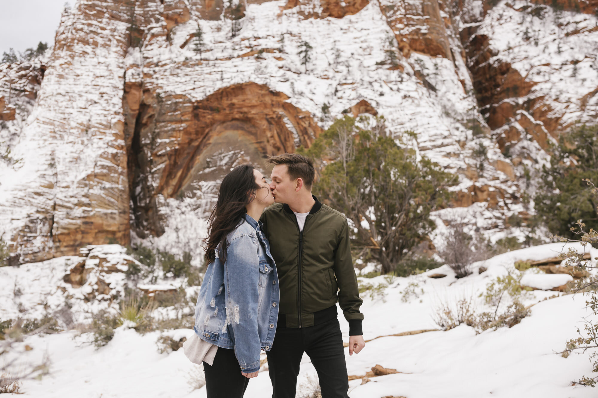 Engagement couple grab a quick kiss in the snow at Zion